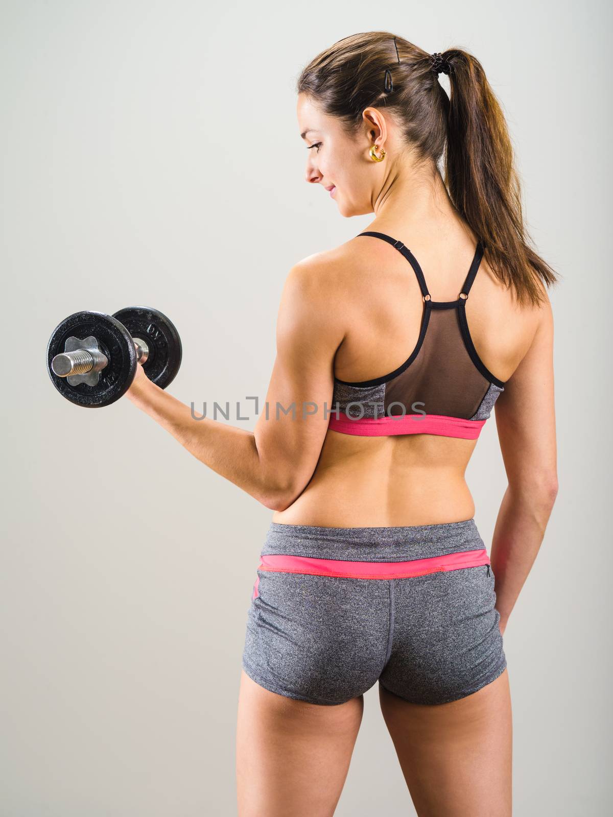Photo of an attractive woman doing a dumbbell curl while standing.
