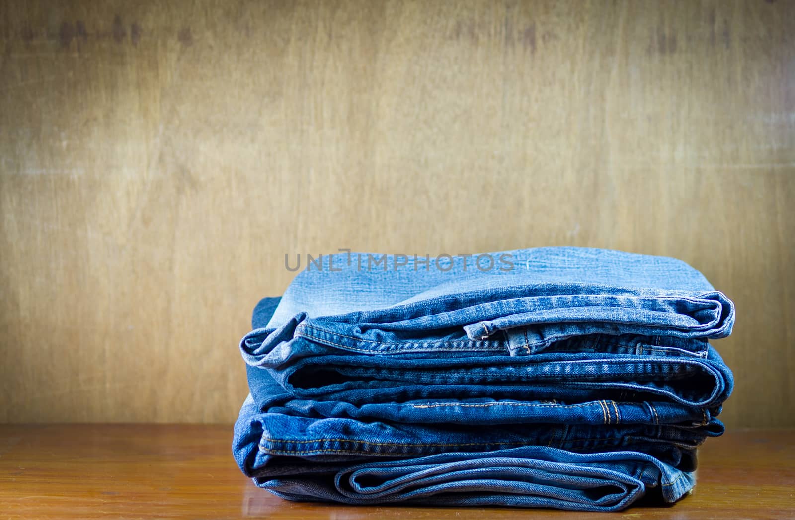 Lot of different old blue jeans on wood background.