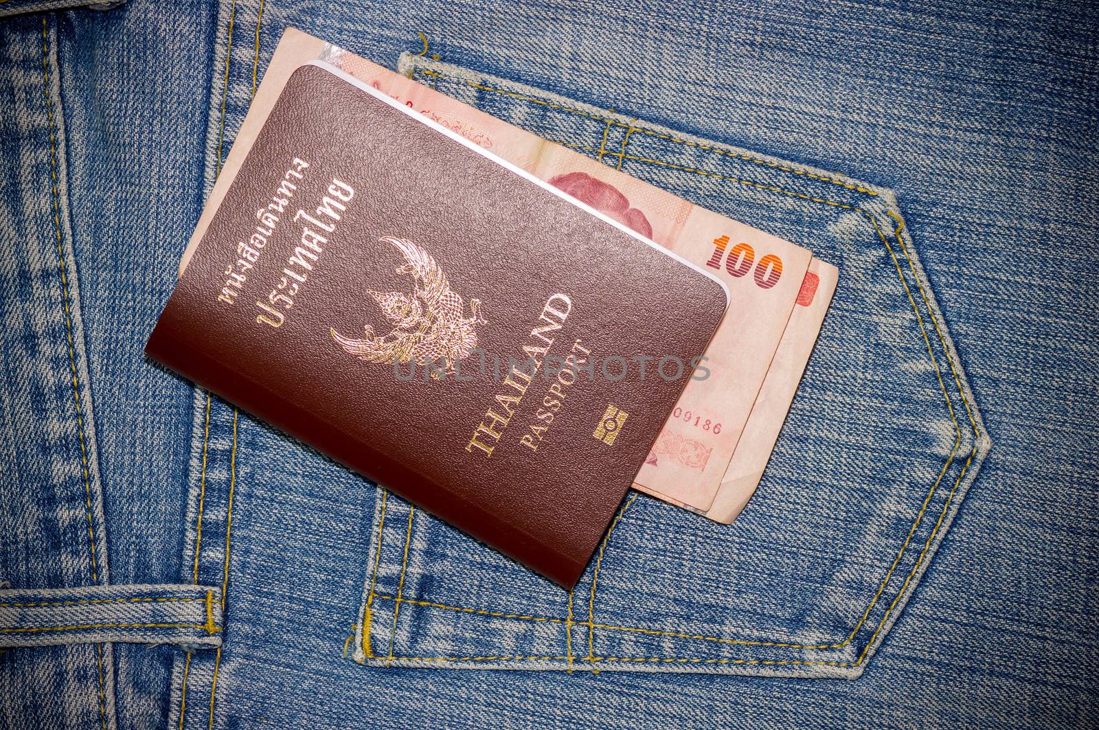 Close up blue jeans pocket with Thailand passport and thai money.