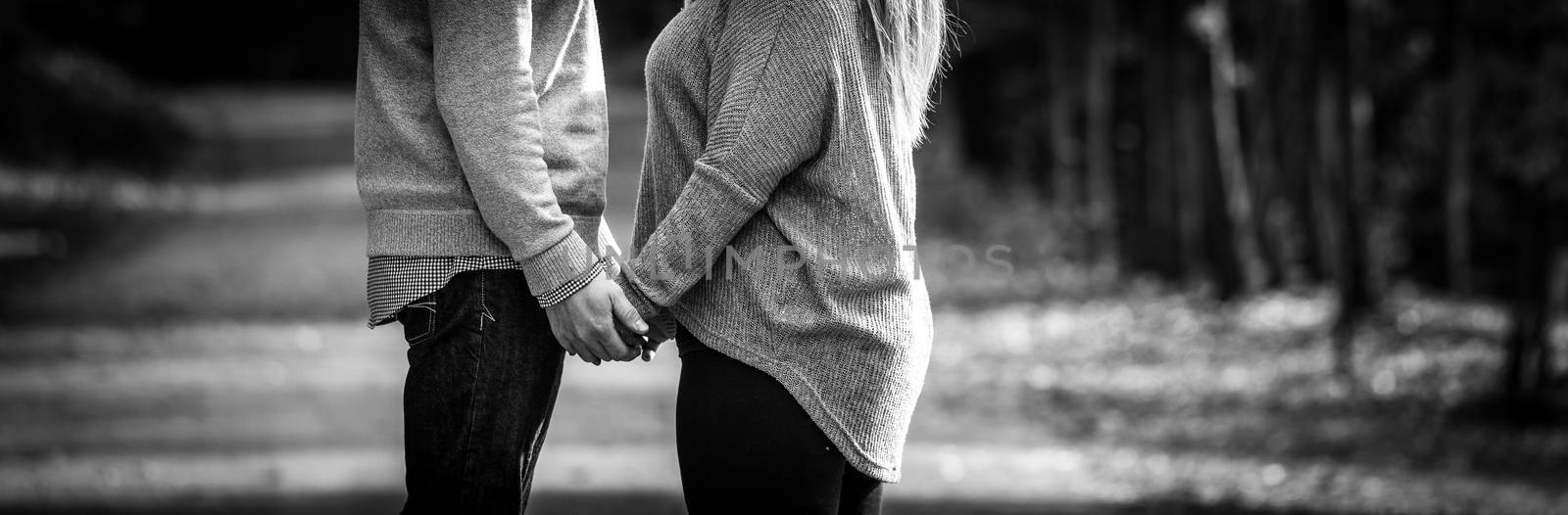 A hopeful young couple holding hands facing each other while stopped during a walk along a country road.