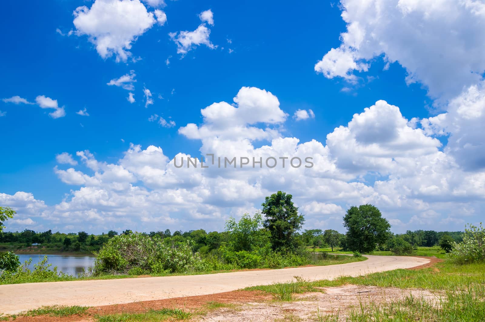 Road through the green field and clouds on blue sky.