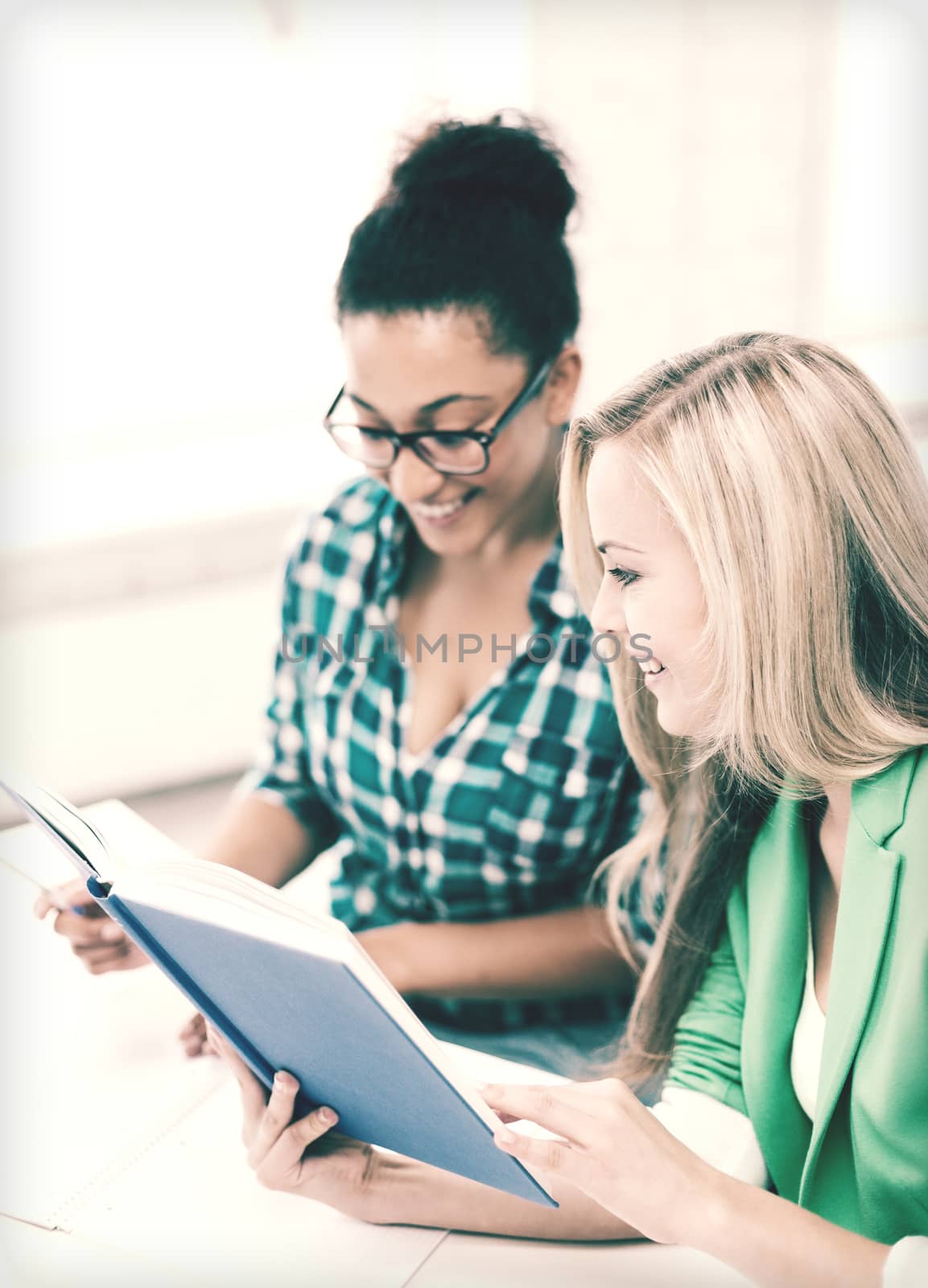 smiling student girls reading book at school by dolgachov