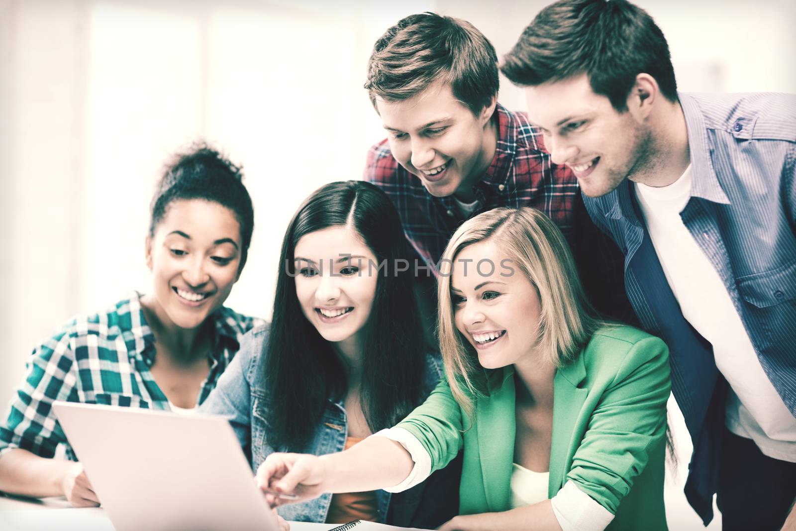 smiling students looking at laptop at school by dolgachov