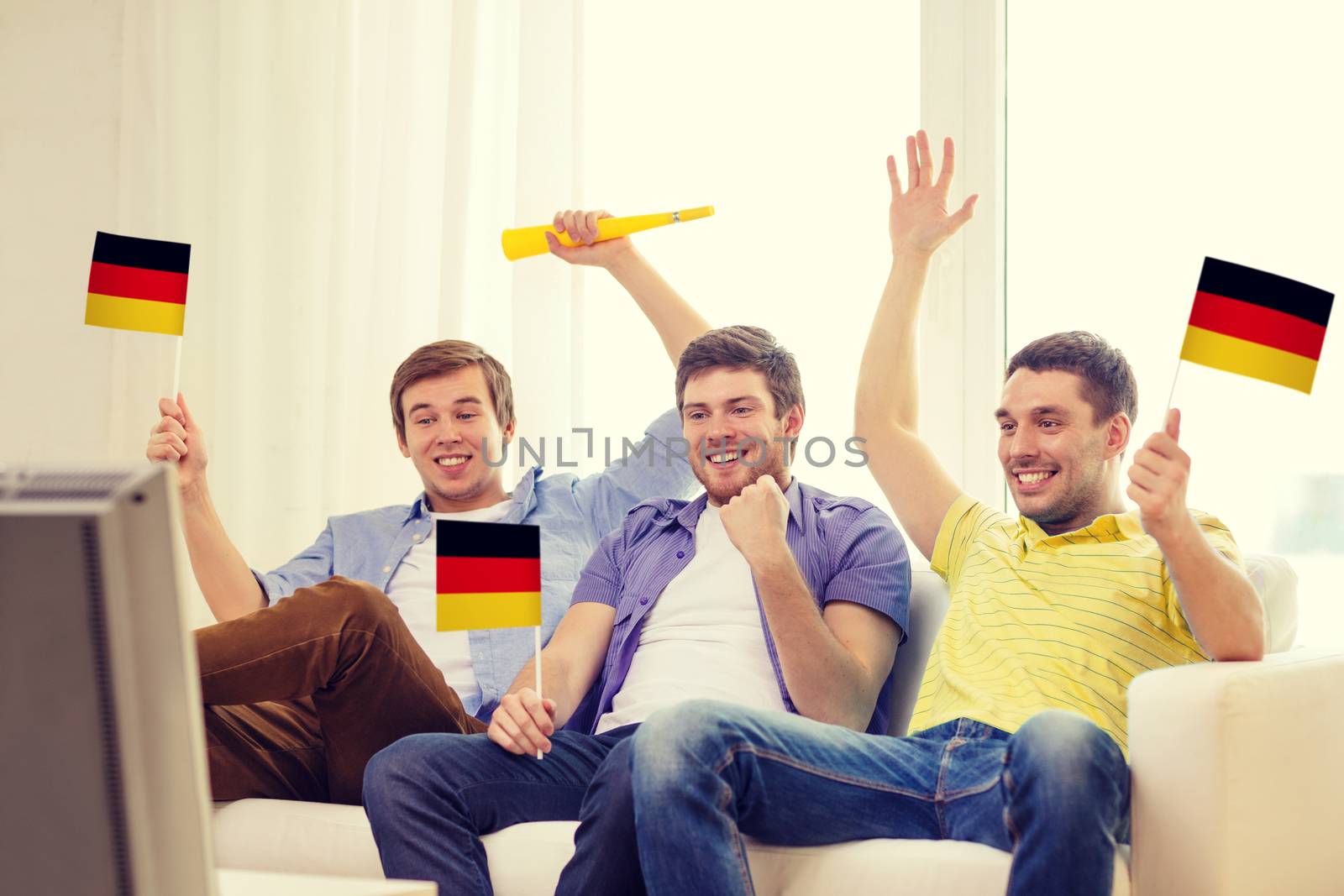 friendship, sports and entertainment concept - happy male friends with flags and vuvuzela supporting football team at home