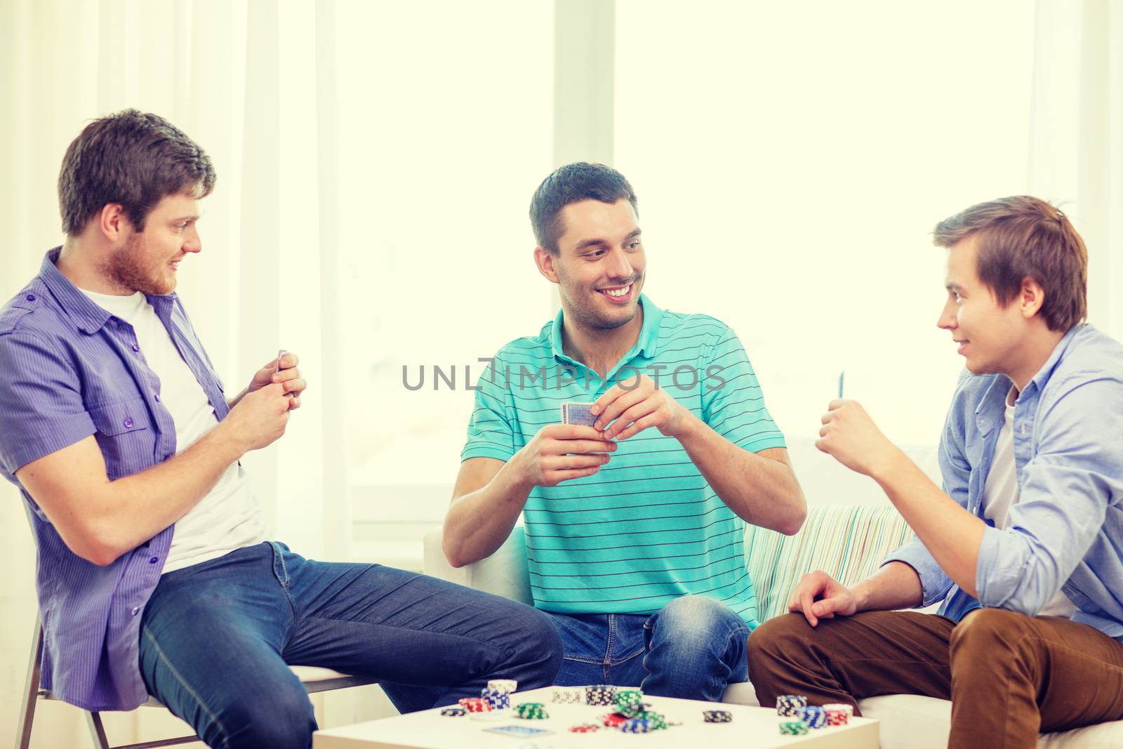 leisure, games and lifestyle concept - happy three male friends playing poker at home