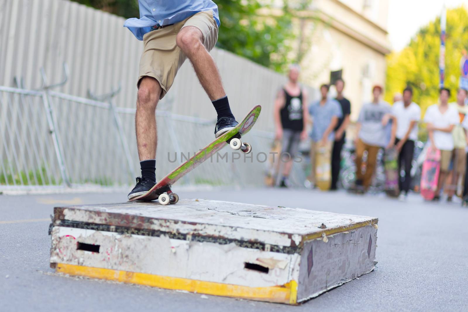 Young skateboarder skateboarding on the street. Skateboarding legs doing slide trick on object. Group of friends cheering in the background.
