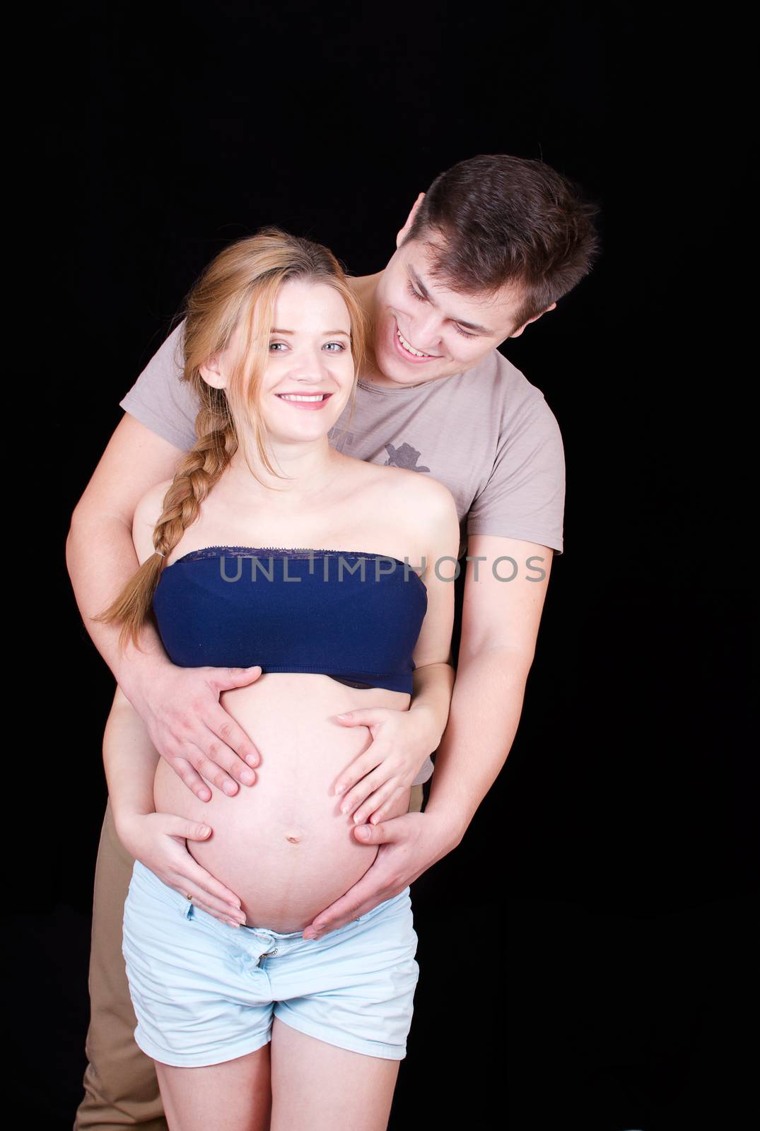 Husband hugs his wife holding his belly where a baby grows