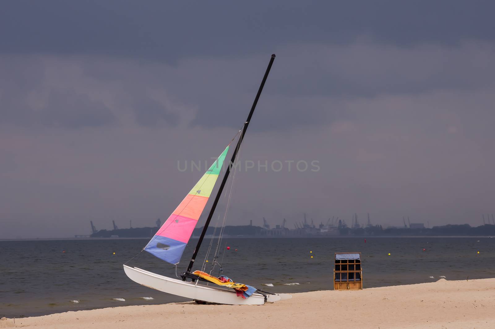 Colorful sailboat on the beach in Sopot, Poland, with the stormy clouds and Gdansk Shipyard in the background.