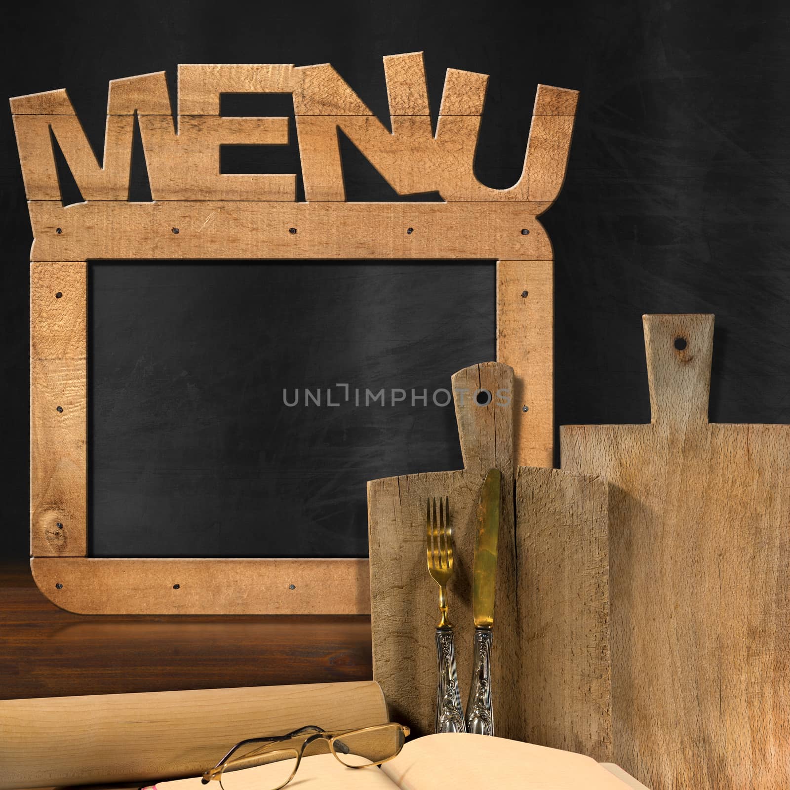 Empty blackboard with wooden frame and text Menu in the kitchen with cutting boards, silver cutlery, recipe book, eyeglasses and rolling pin. Template for food menu