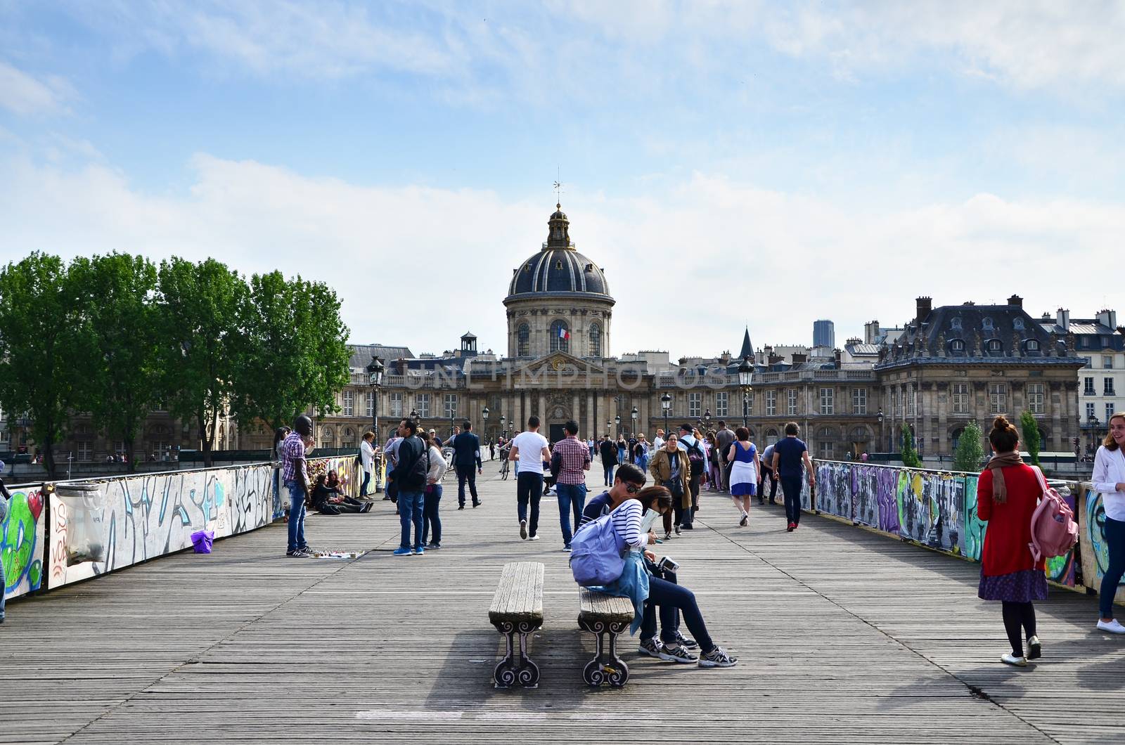 Paris, France - May 13, 2015: People visit Institut de France and the Pont des Arts or Passerelle des Arts bridge across river Seine in Paris, France. on May 13, 2015.