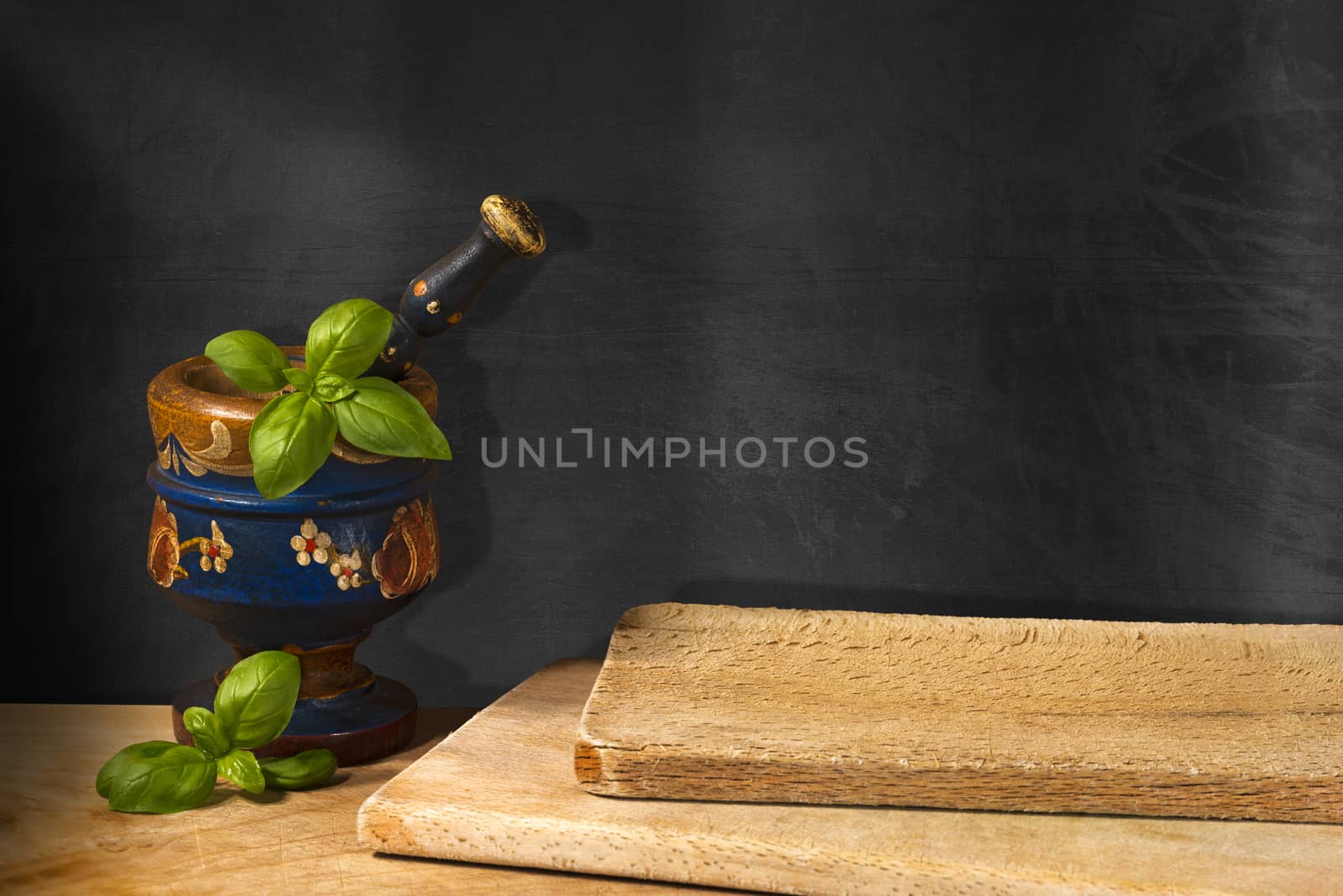 Empty blackboard on the wall, old wooden mortar and pestle with basil leaves. Concept of rustic cuisine