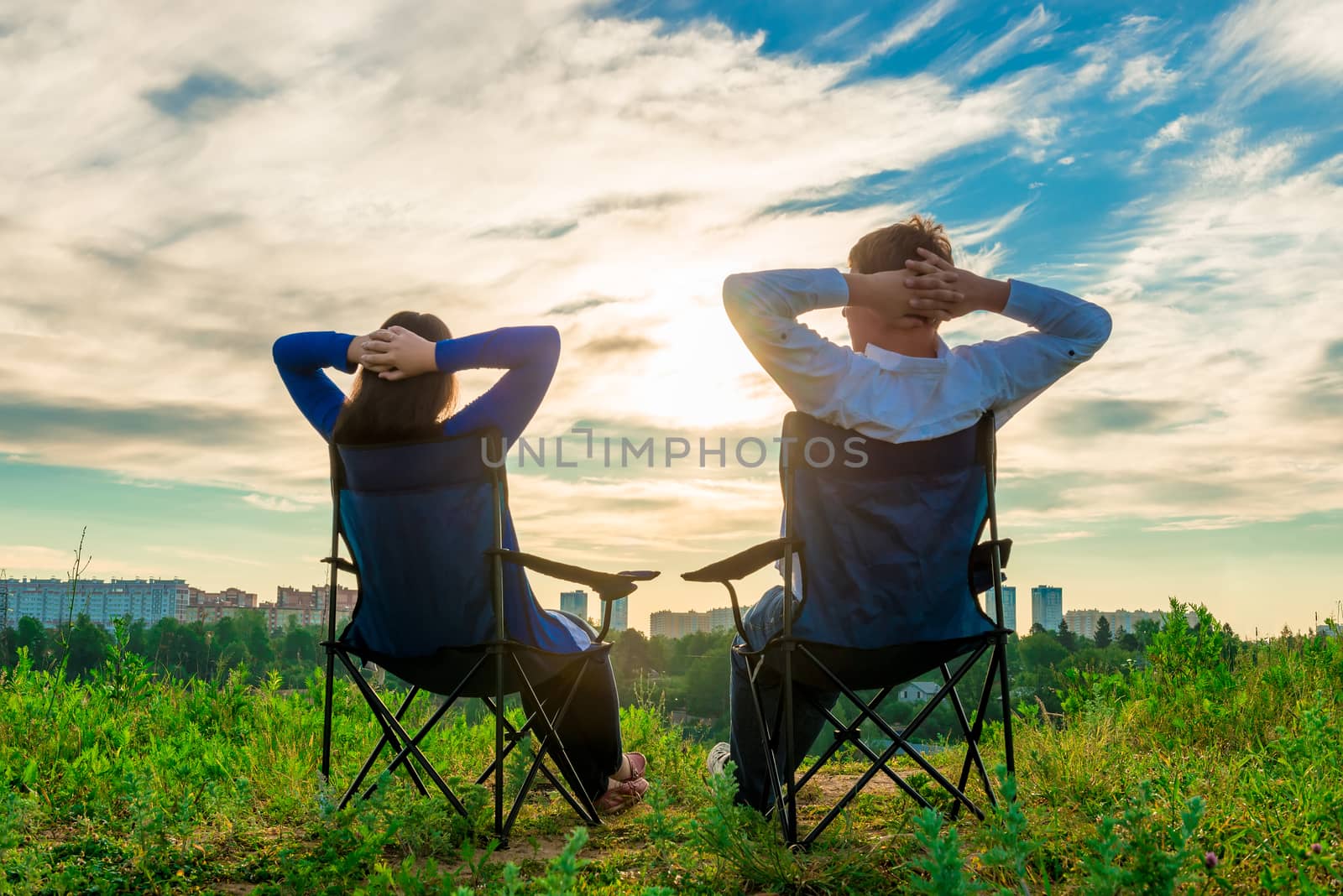 man and woman sitting in chairs and admire the sunrise over the city