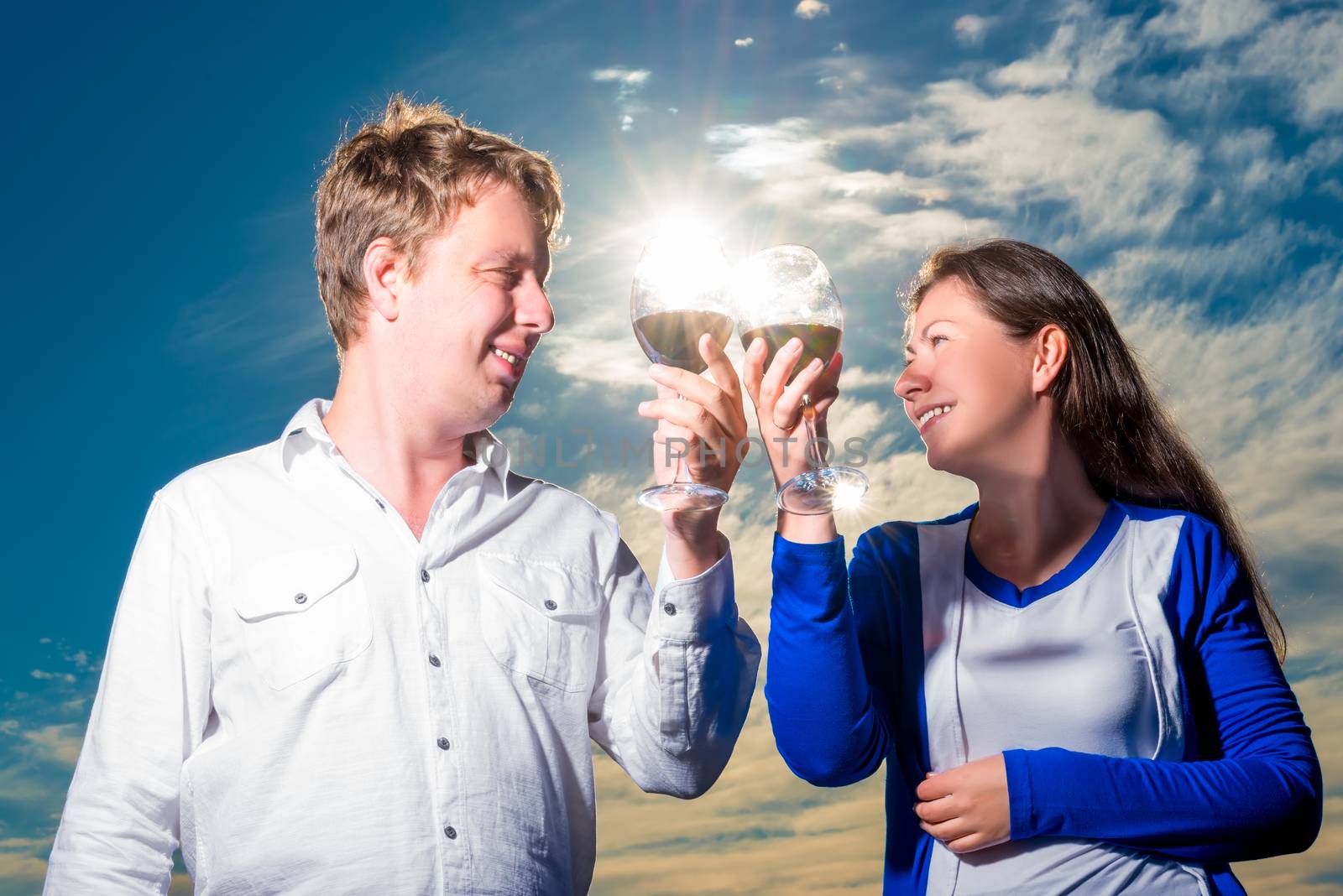 happy couple with glasses of wine in solar beams