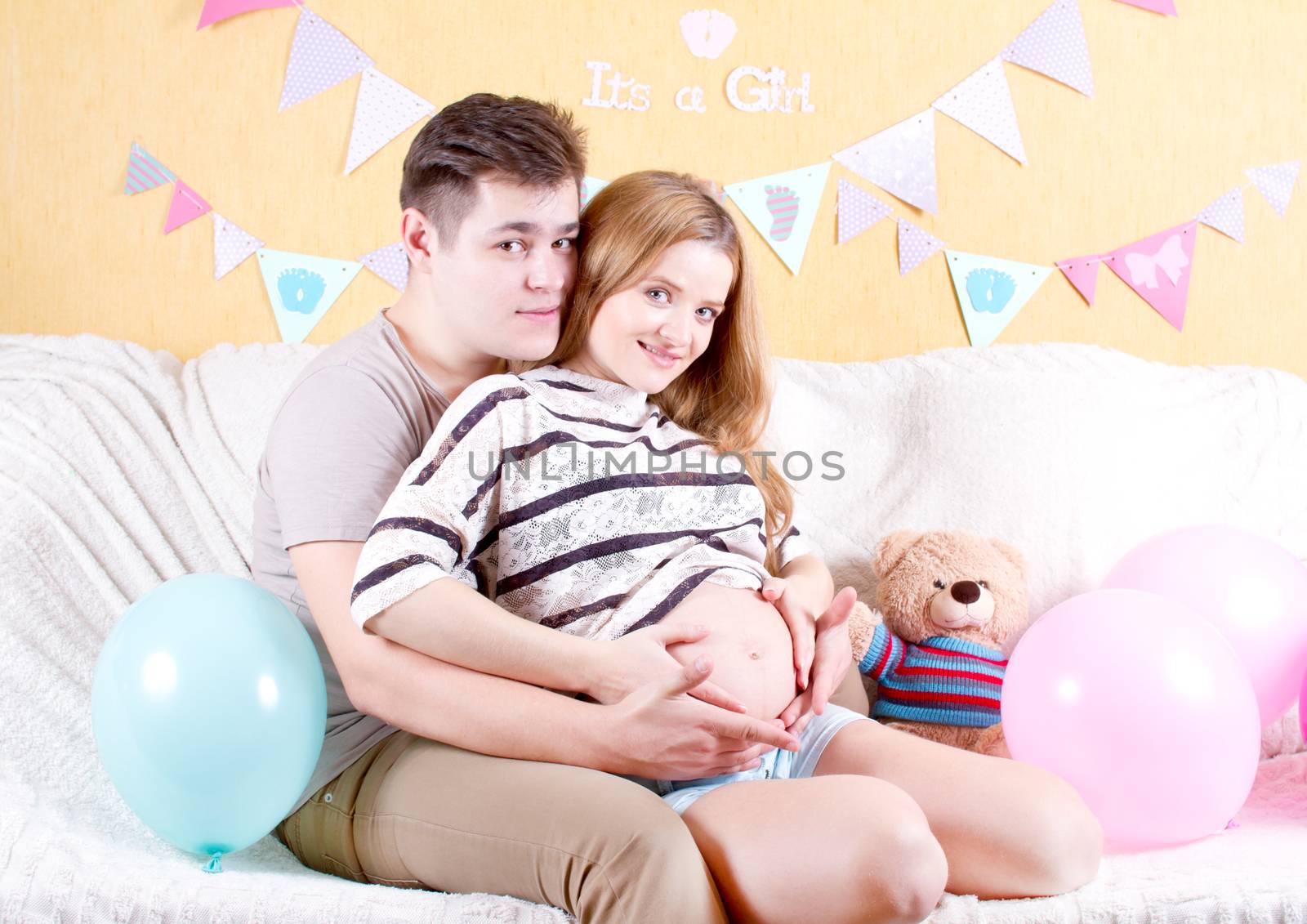 Man and a pregnant woman sitting on the sofa hugging his stomach belly