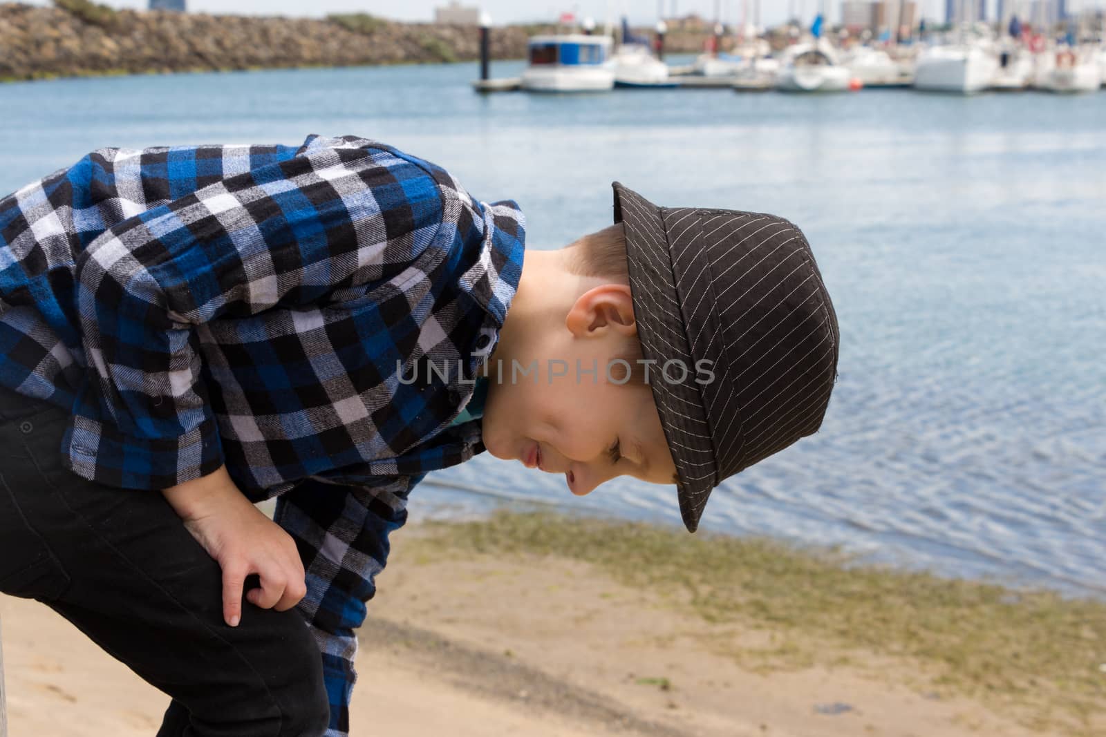 A young boy bending over to pick up rocks at the beach.