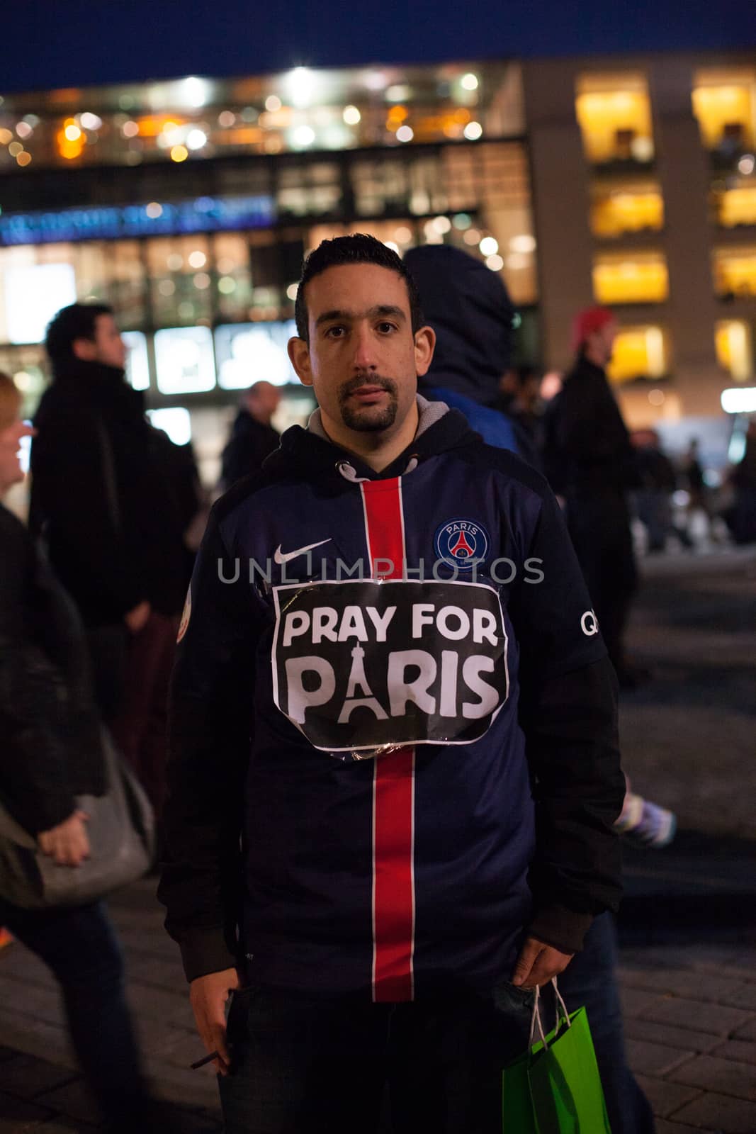 GERMANY, Berlin: A man wearing a sign reading Pray for Paris gathers with others outside the French Embassy in Berlin while the nearby Brandenburg Gate is illuminated with the colours of the French flag on November 14, 2015, the day after a series of terror attacks in Paris. Islamic State has claimed responsibility for the attacks, which killed at least 129 people and left hundreds more injured in scenes of carnage at a concert hall, restaurants and the national stadium on Friday, November 13.