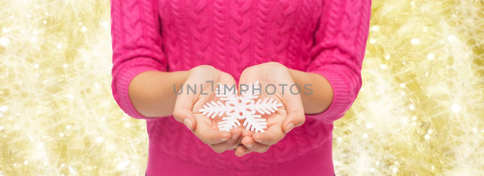 christmas, holidays and people concept - close up of woman in pink sweater holding snowflake over yellow background