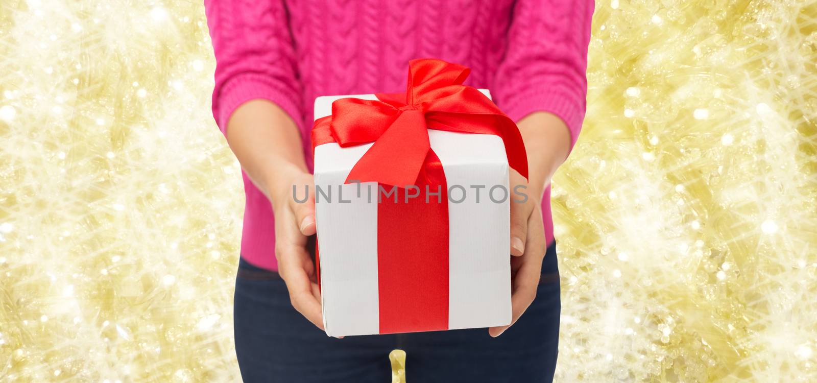 christmas, holidays and people concept - close up of woman in pink sweater holding gift box over yellow background