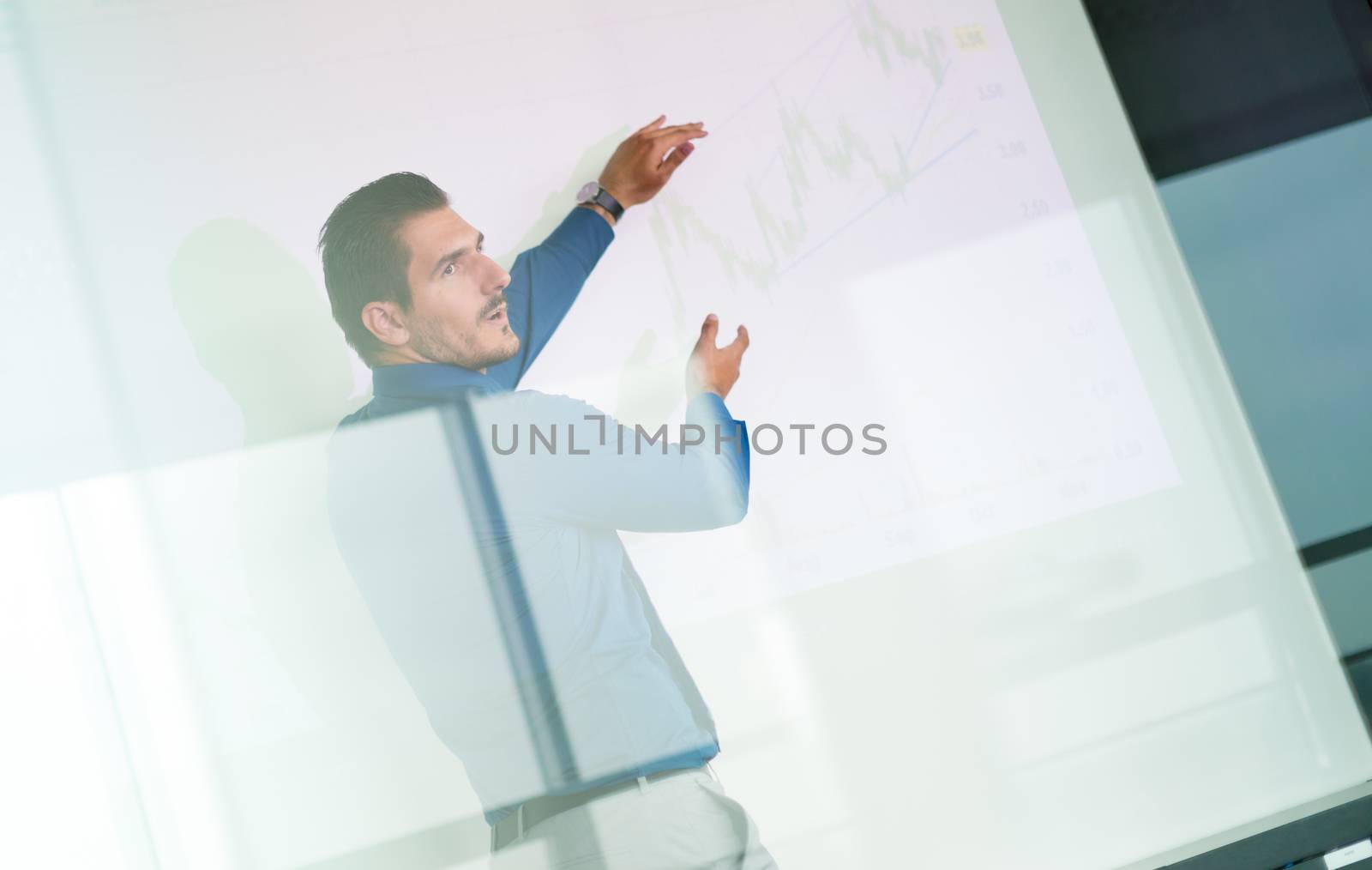 Business man making a presentation in front of whiteboard. Business executive delivering a presentation to his colleagues during meeting or in-house business training. View through glass.