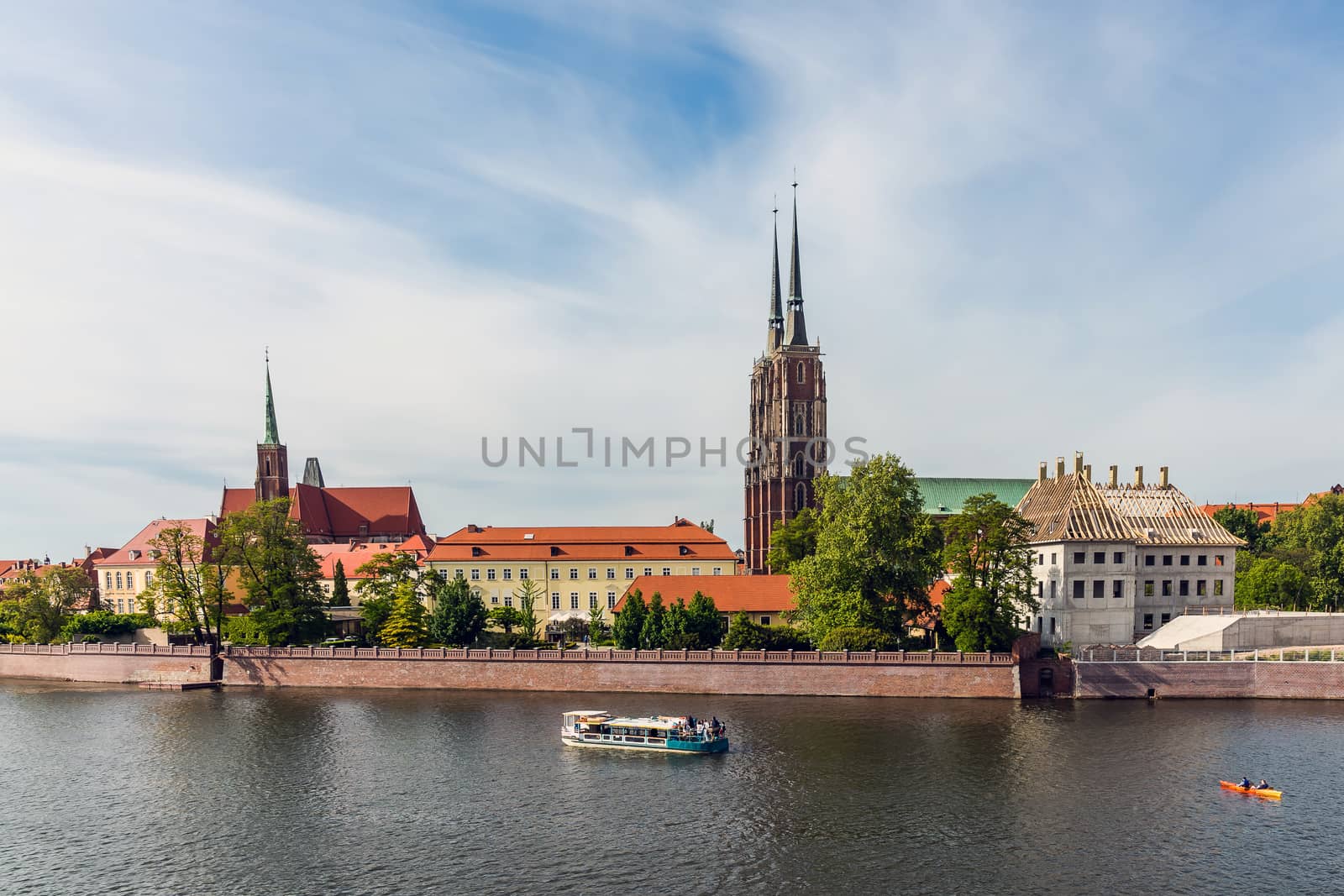 Pleasure boat and canoe on the Oder river in Wroclaw by the Ostrow Tumski, the oldest part of the city with The Cathedral of St. John the Baptist and The Church of the Holy Cross.