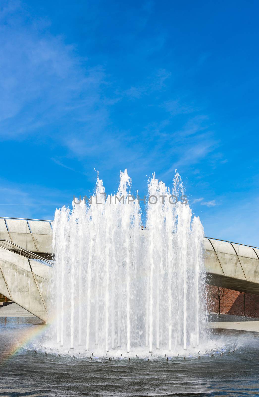 Water fountain at the blue sky preceded by the rainbow.