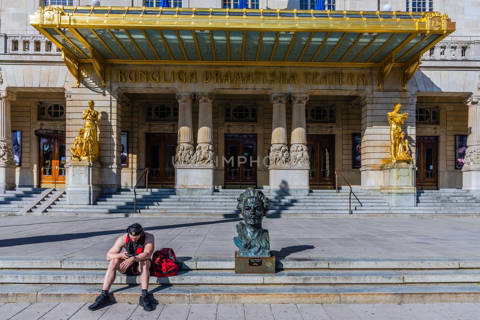 Unidentified passerby sits by the August Strindberg bust in front of the Royal Dramatic Theater in Stockholm. The theatre is located in the Art Nouveau building at Nybroplan since 1908