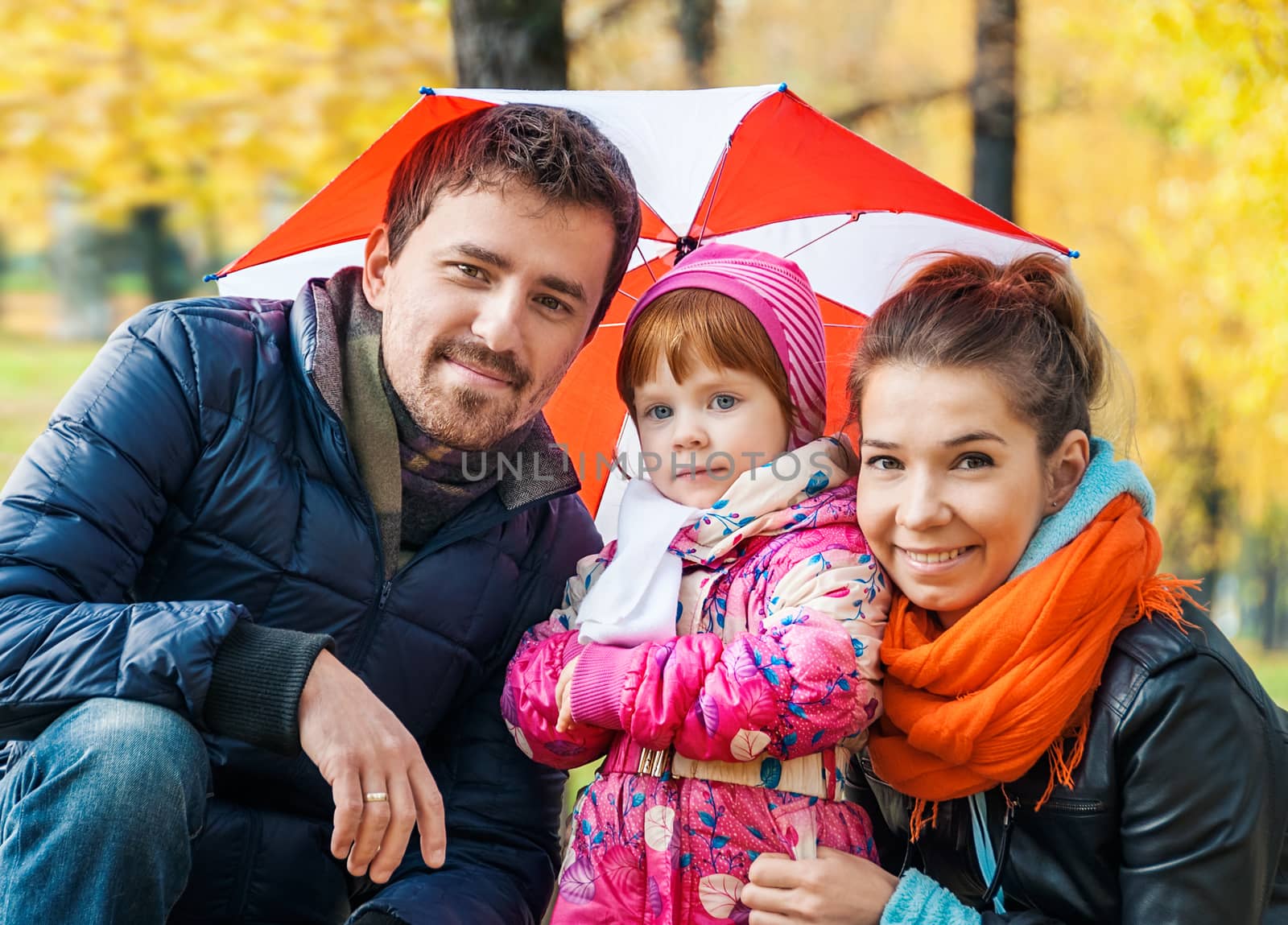 Happy young family under an umbrella in an autumn park by zeffss