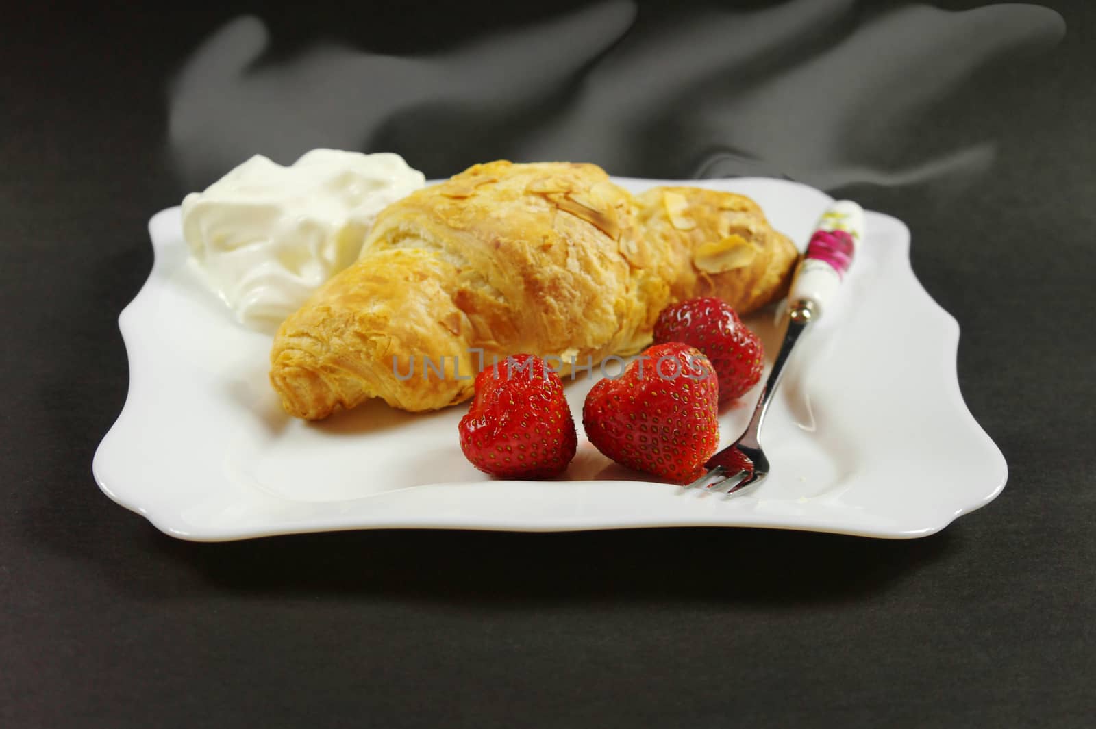 hot croissant with a strawberries on plate against the black background