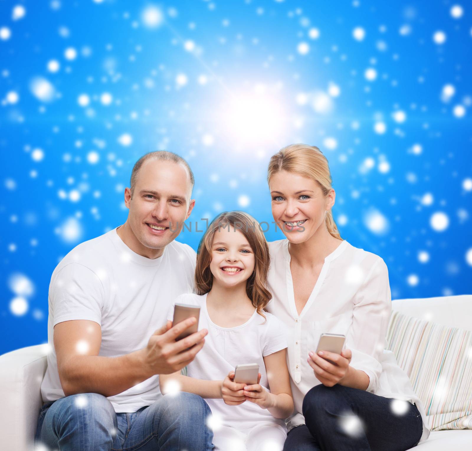 family, christmas holidays, technology and people concept - smiling mother, father and little girl with smartphones over blue snowy background