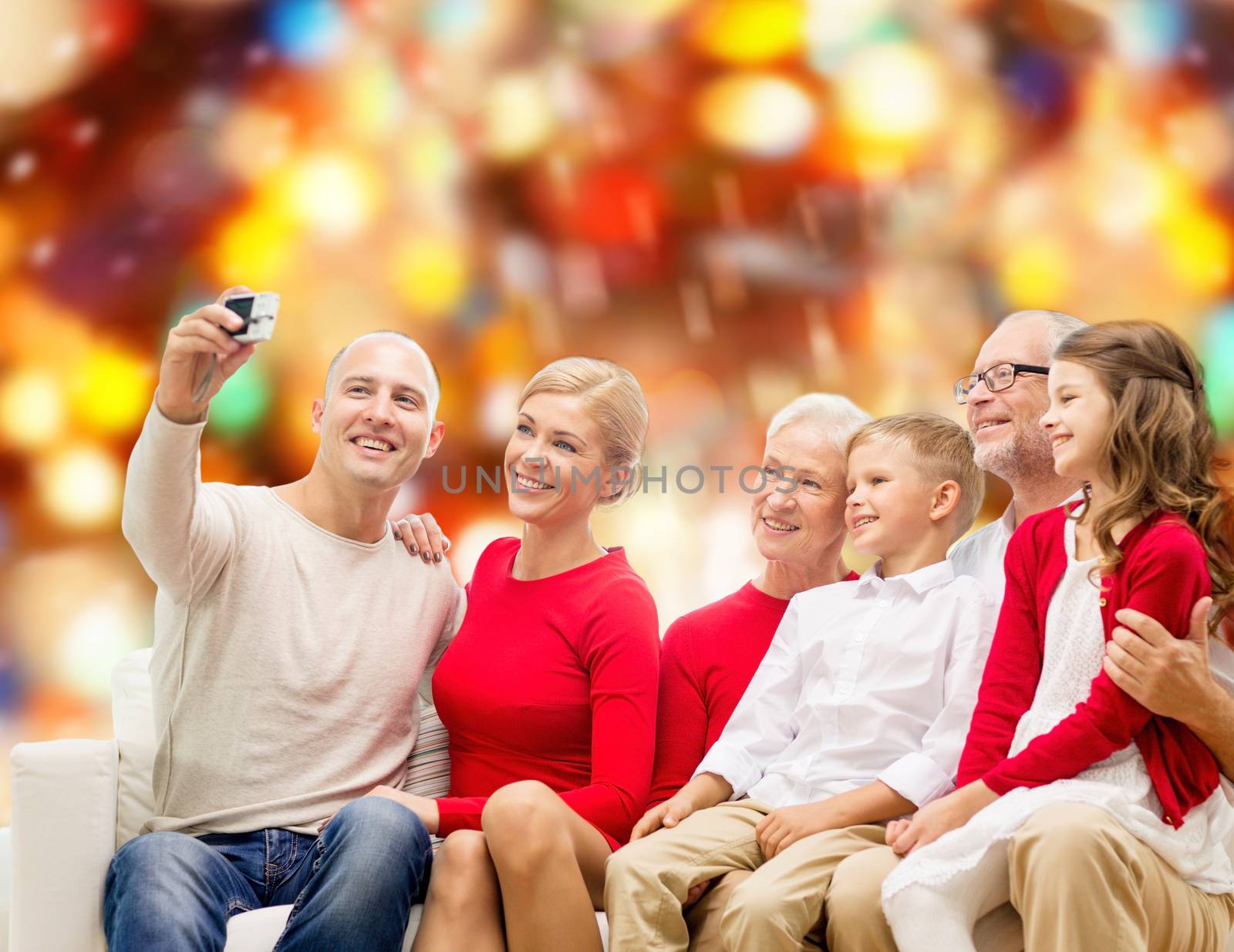 family, holidays, generation, christmas and people concept - smiling family with camera taking selfie and sitting on couch over red lights background