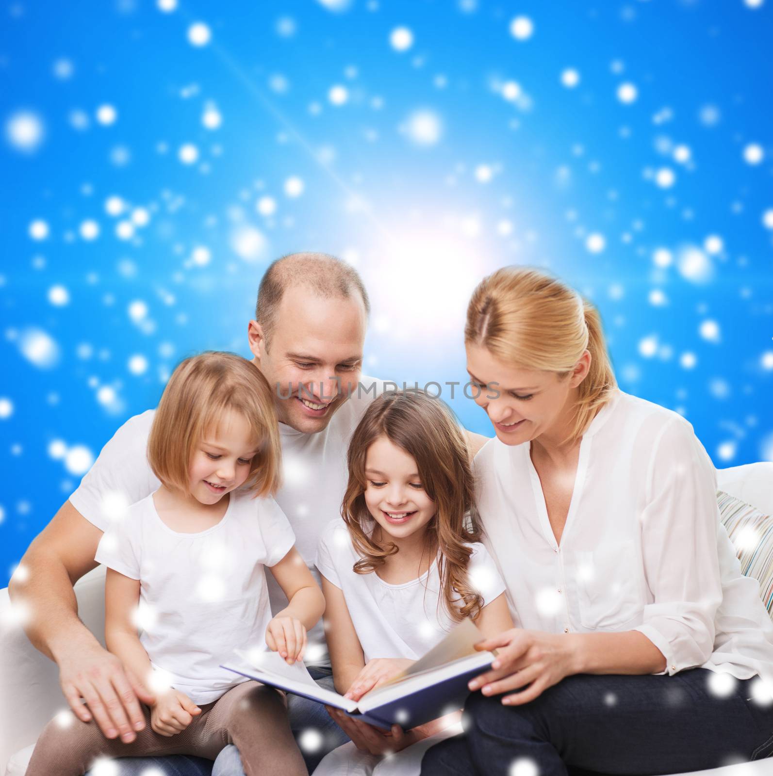 family, childhood, christmas holidays and people - smiling mother, father and little girls reading book over blue snowy background