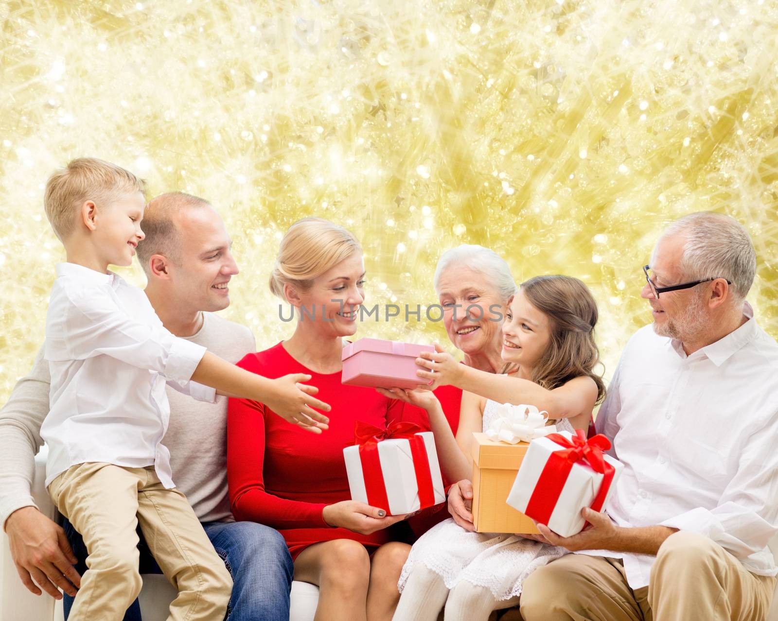 family, holidays, generation, christmas and people concept - smiling family with gift boxes sitting on couch over yellow lights background