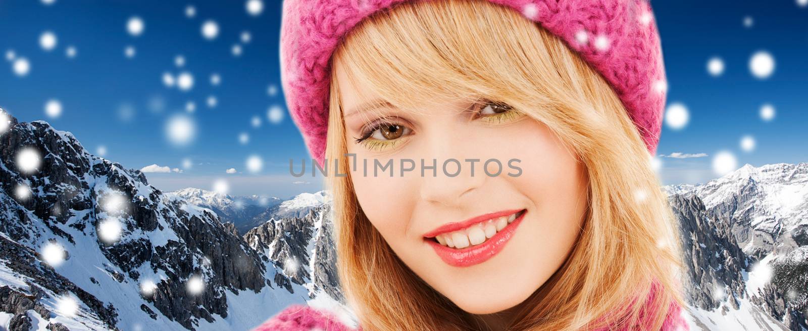 happiness, winter holidays, christmas and people concept - close up of smiling young woman in pink hat and scarf over snowy mountains background