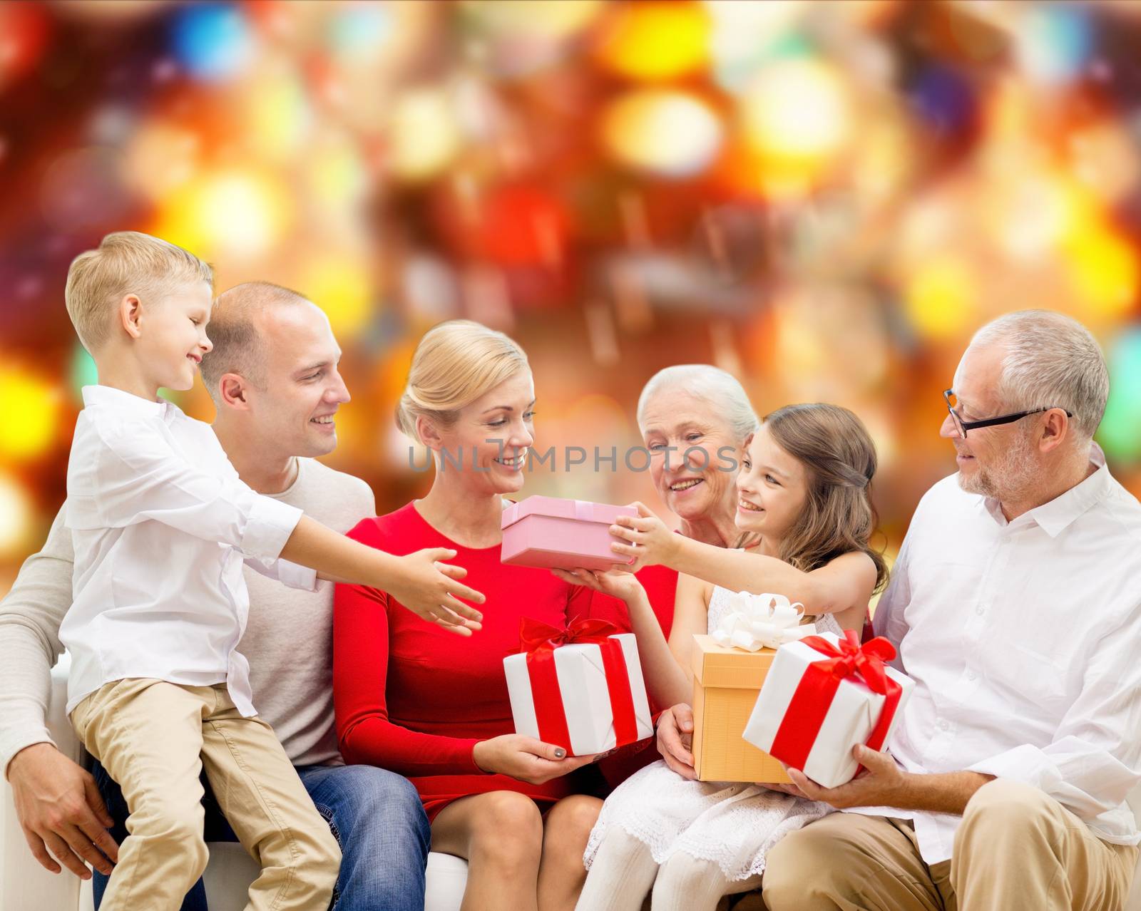 family, holidays, generation, christmas and people concept - smiling family with gift boxes sitting on couch over red lights background