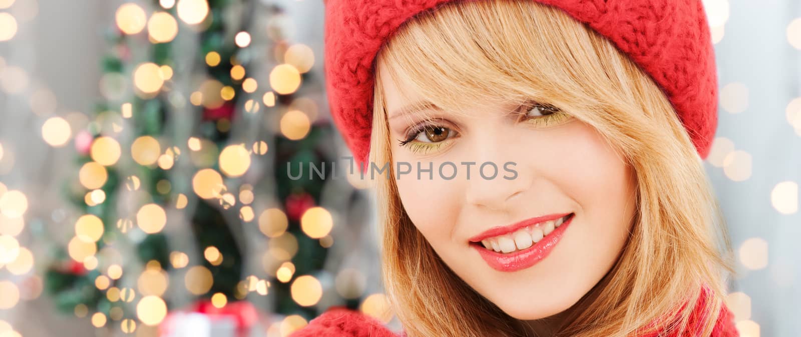 happiness, winter holidays and people concept - close up of smiling young woman in red hat and scarf over christmas tree lights background