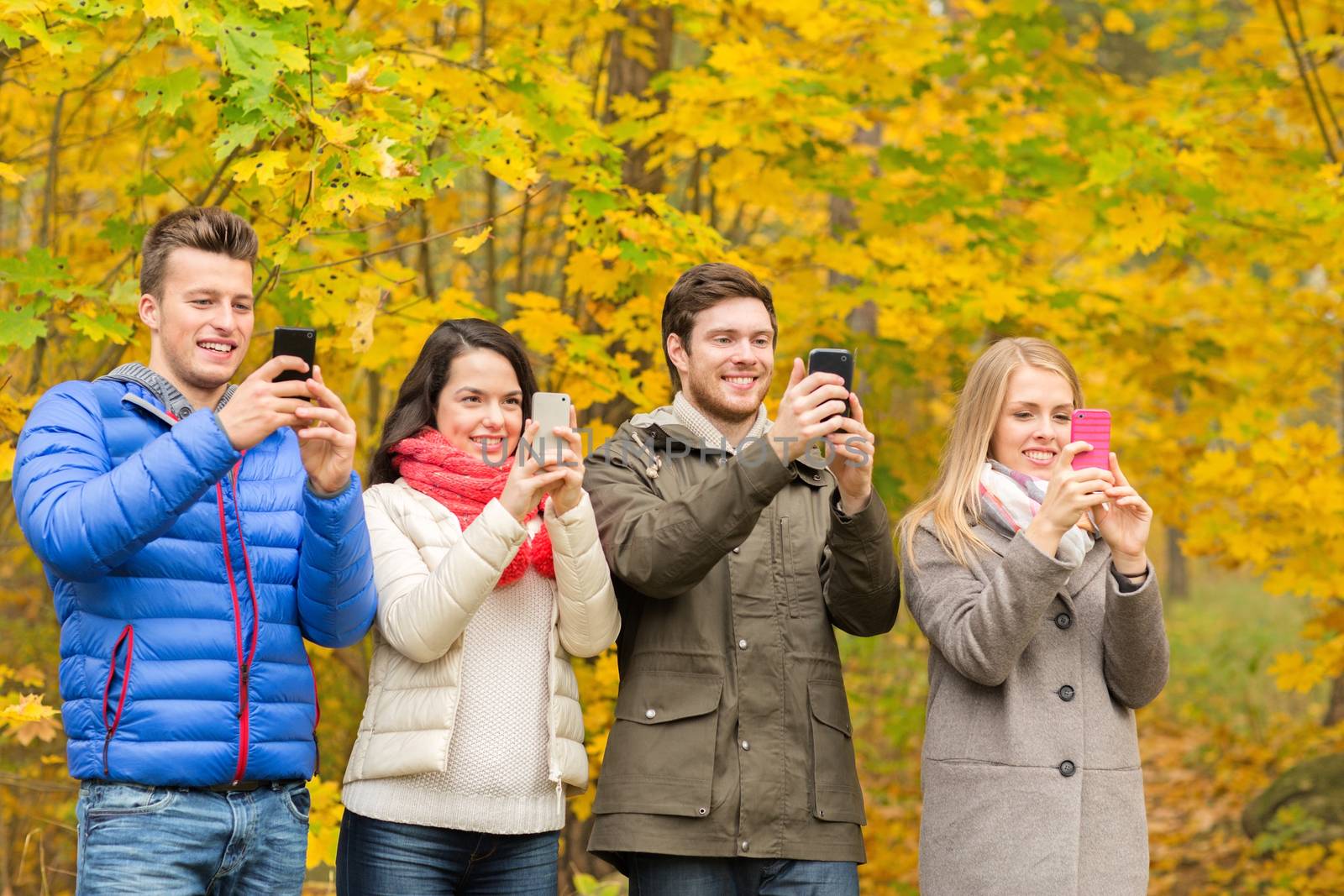 season, people, technology and friendship concept - group of smiling friends with smartphones taking picture in autumn park