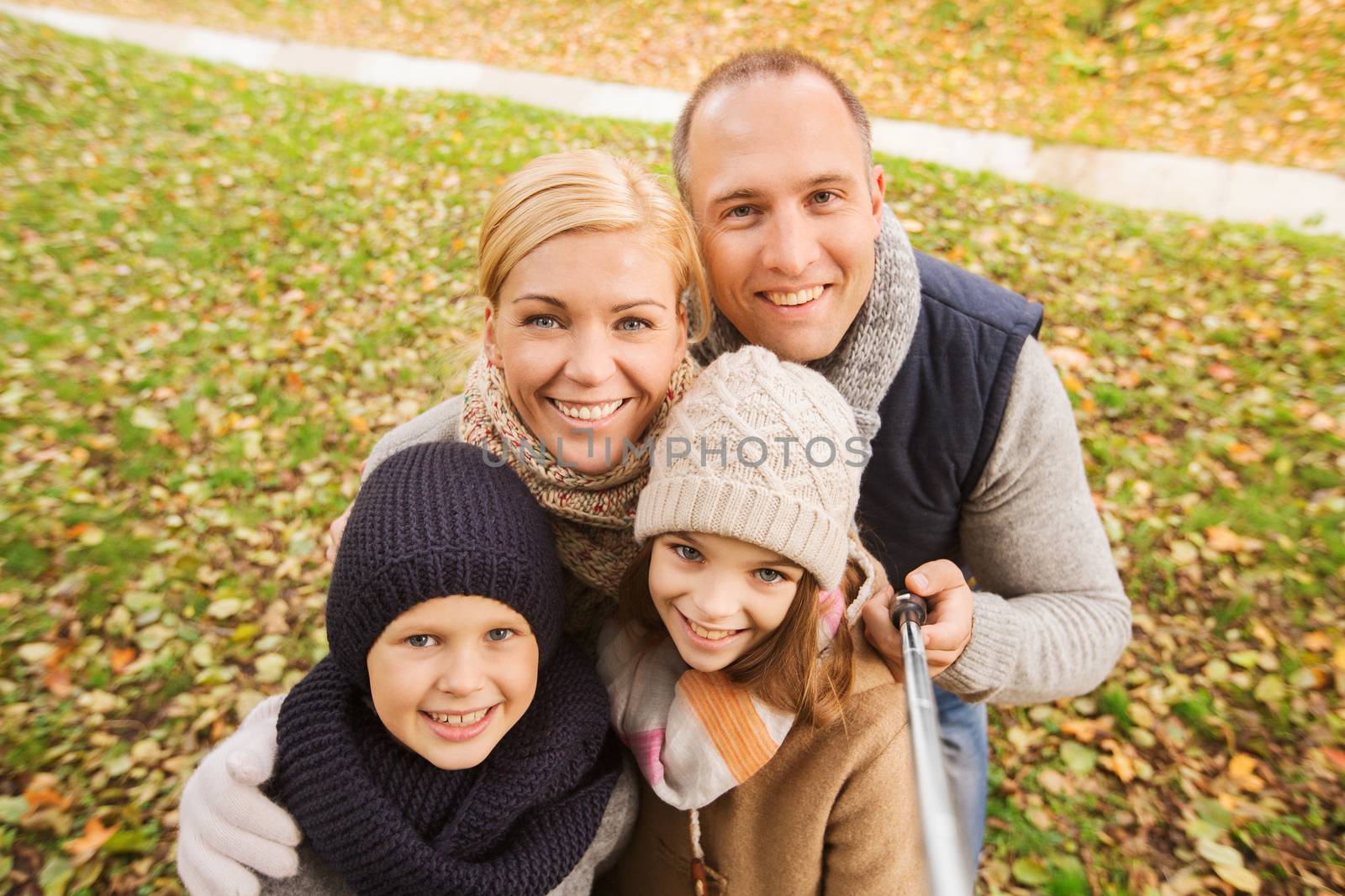 family, childhood, season, technology and people concept - happy family photographing with selfie stick in autumn park