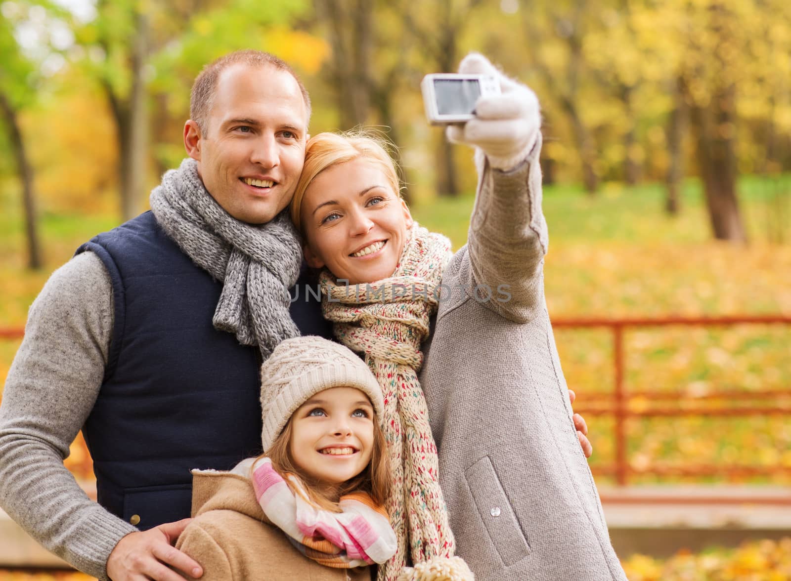 family, childhood, season, technology and people concept - happy family taking selfie with smartphone in autumn park