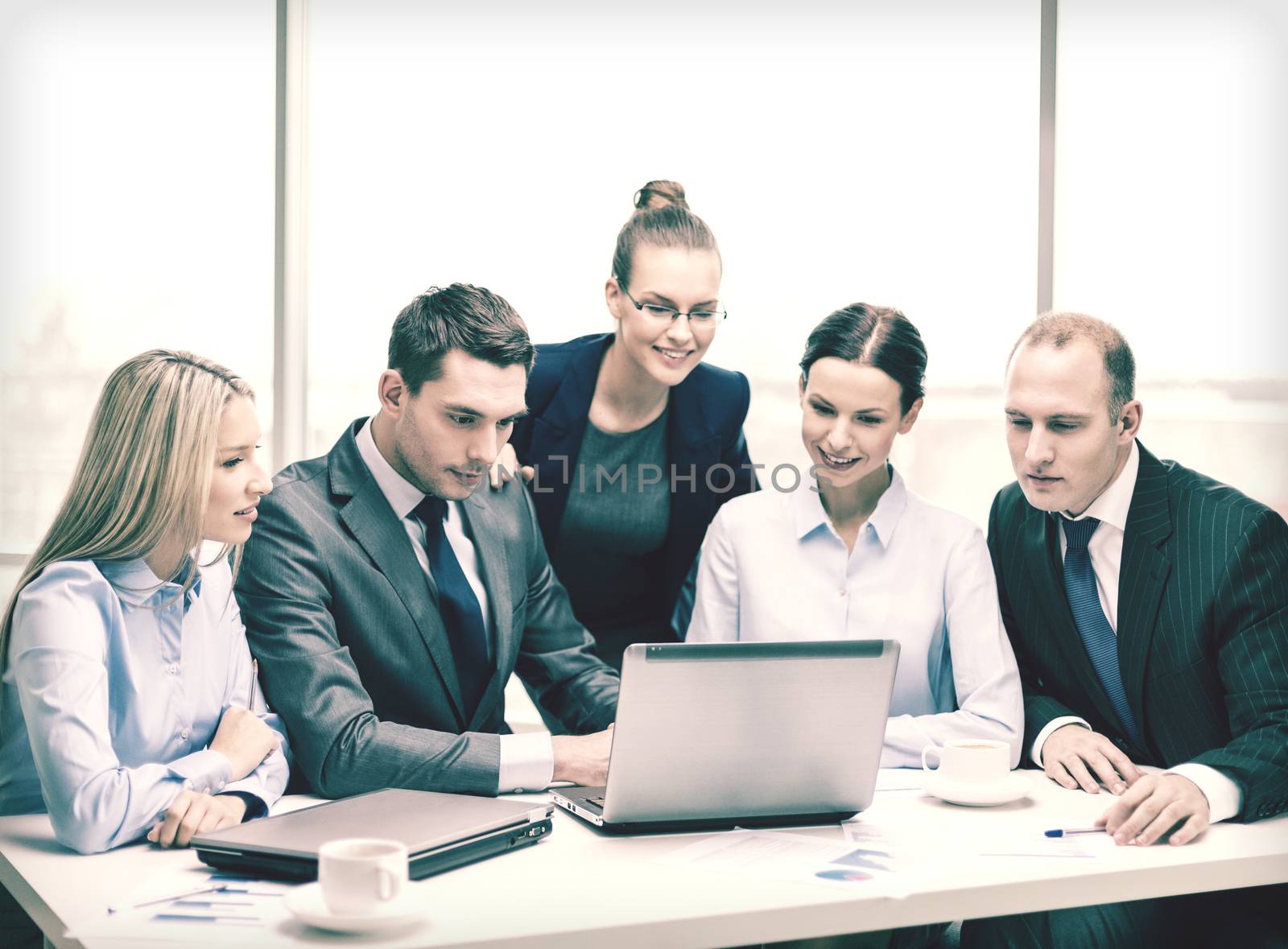 business, technology and office concept - smiling business team with laptop computers, documents and coffee having discussion in office