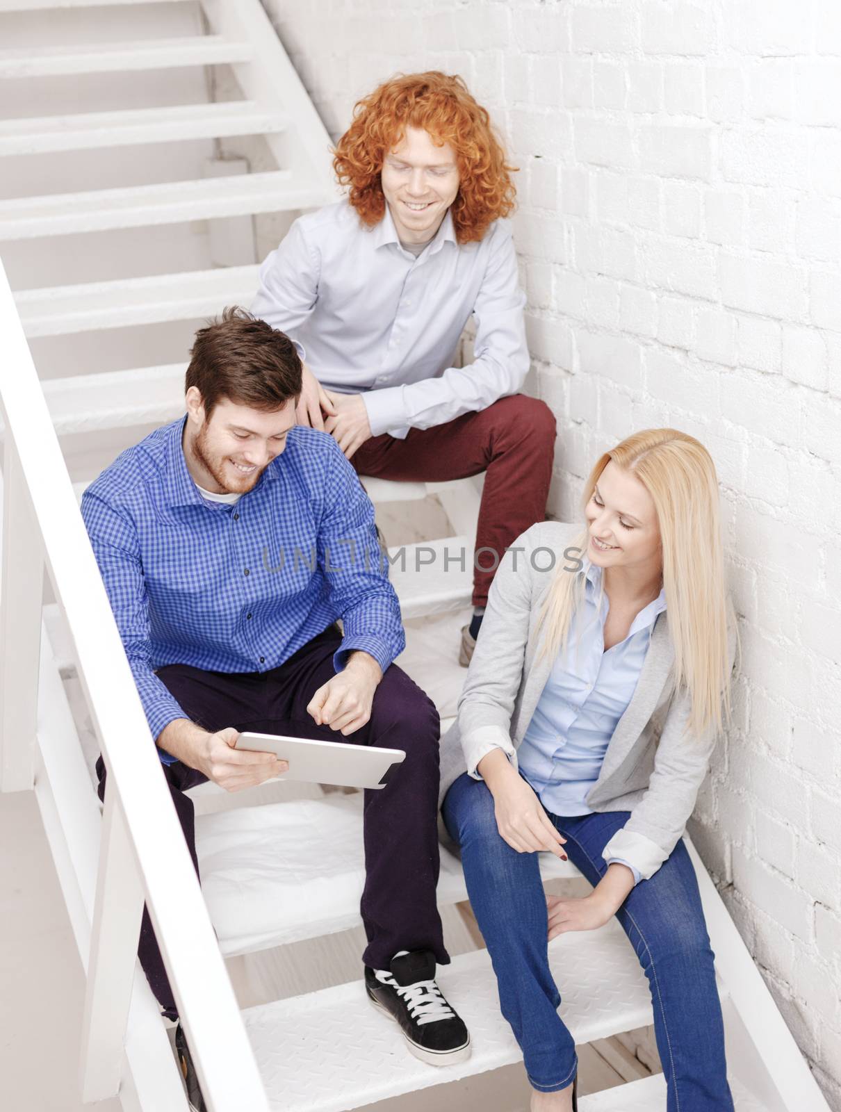 business, technology and startup concept - smiling creative team with tablet pc computer sitting on staircase