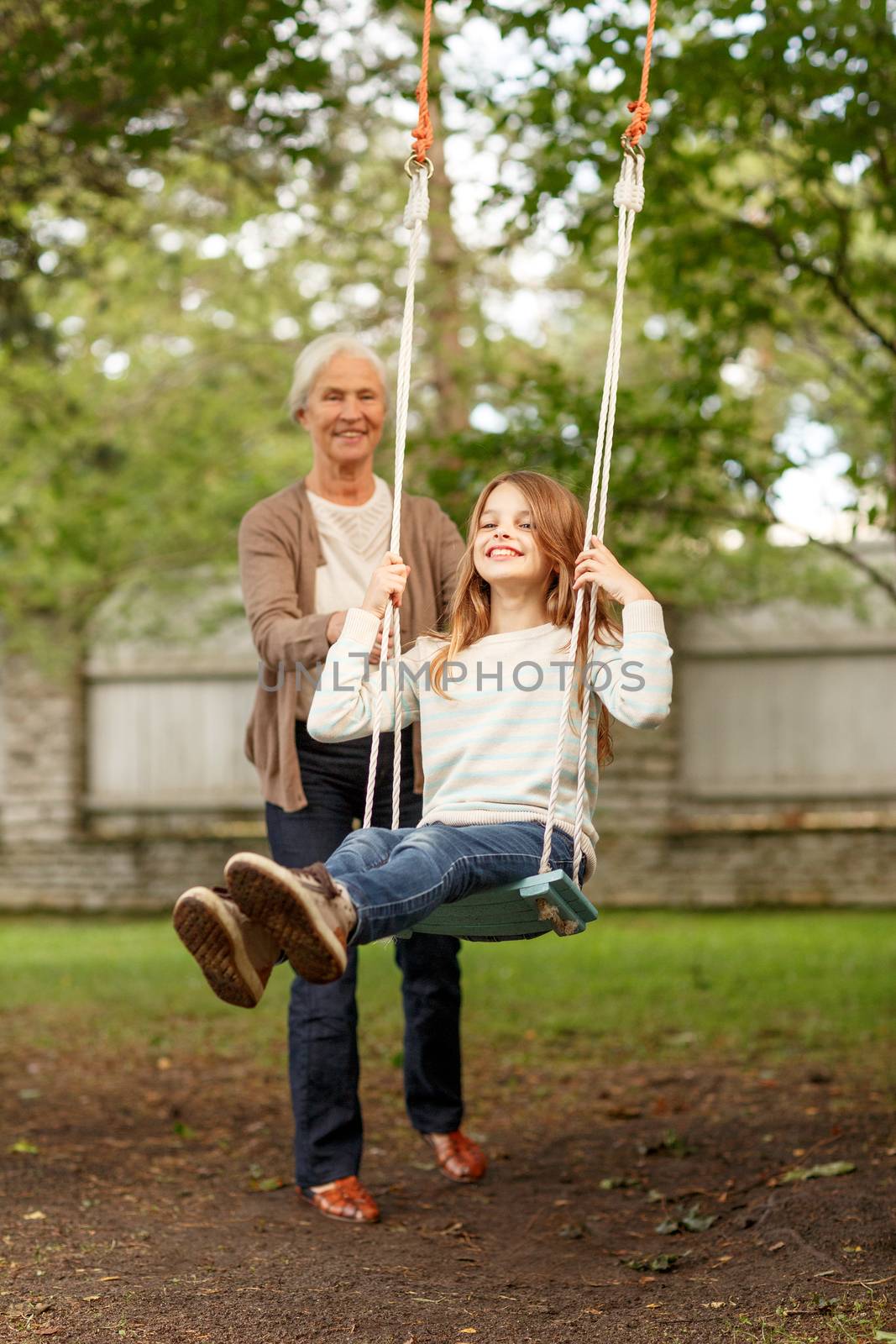 family, happiness, generation, home and people concept - happy grandmother and granddaughter swinging on teeterboard outdoors