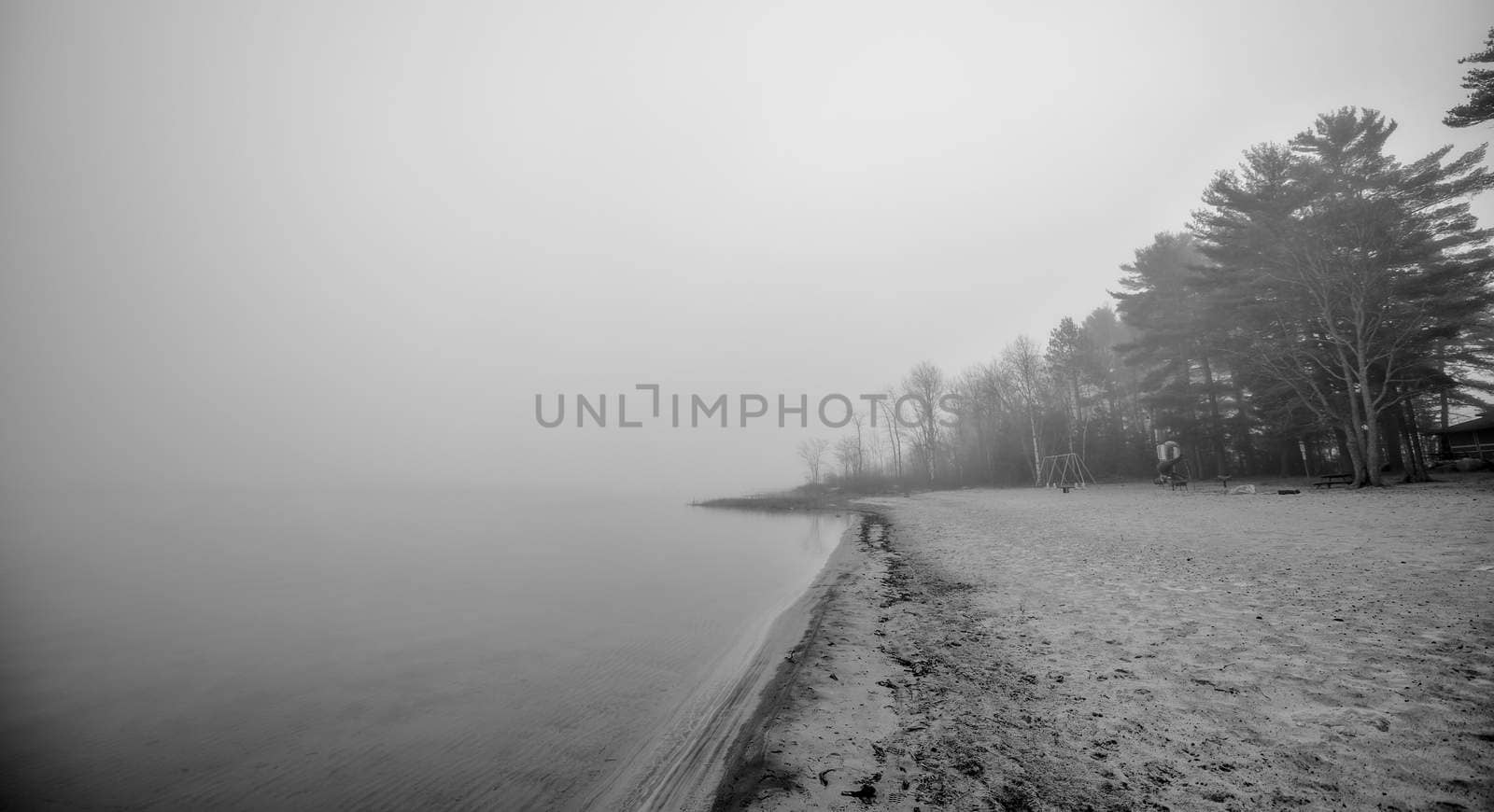 Black & white of lonely empty beach in November autumn fog in Ontario Canada.