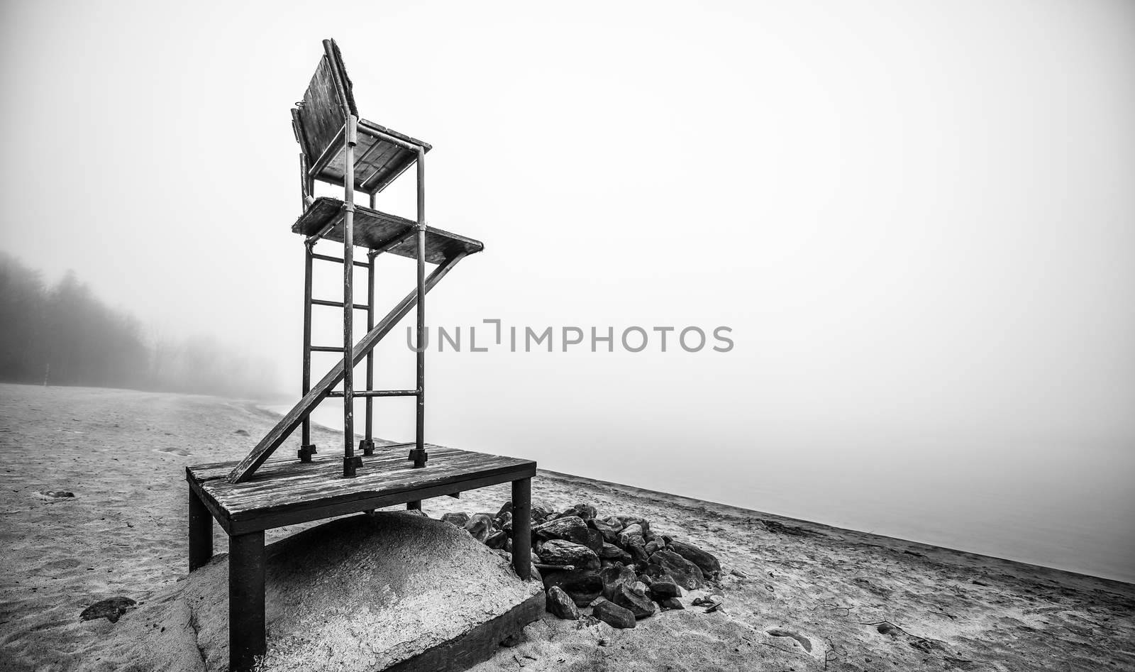 Black & white of lonely lifeguard seat stands empty in the fog on a November beach in Ontario Canada.