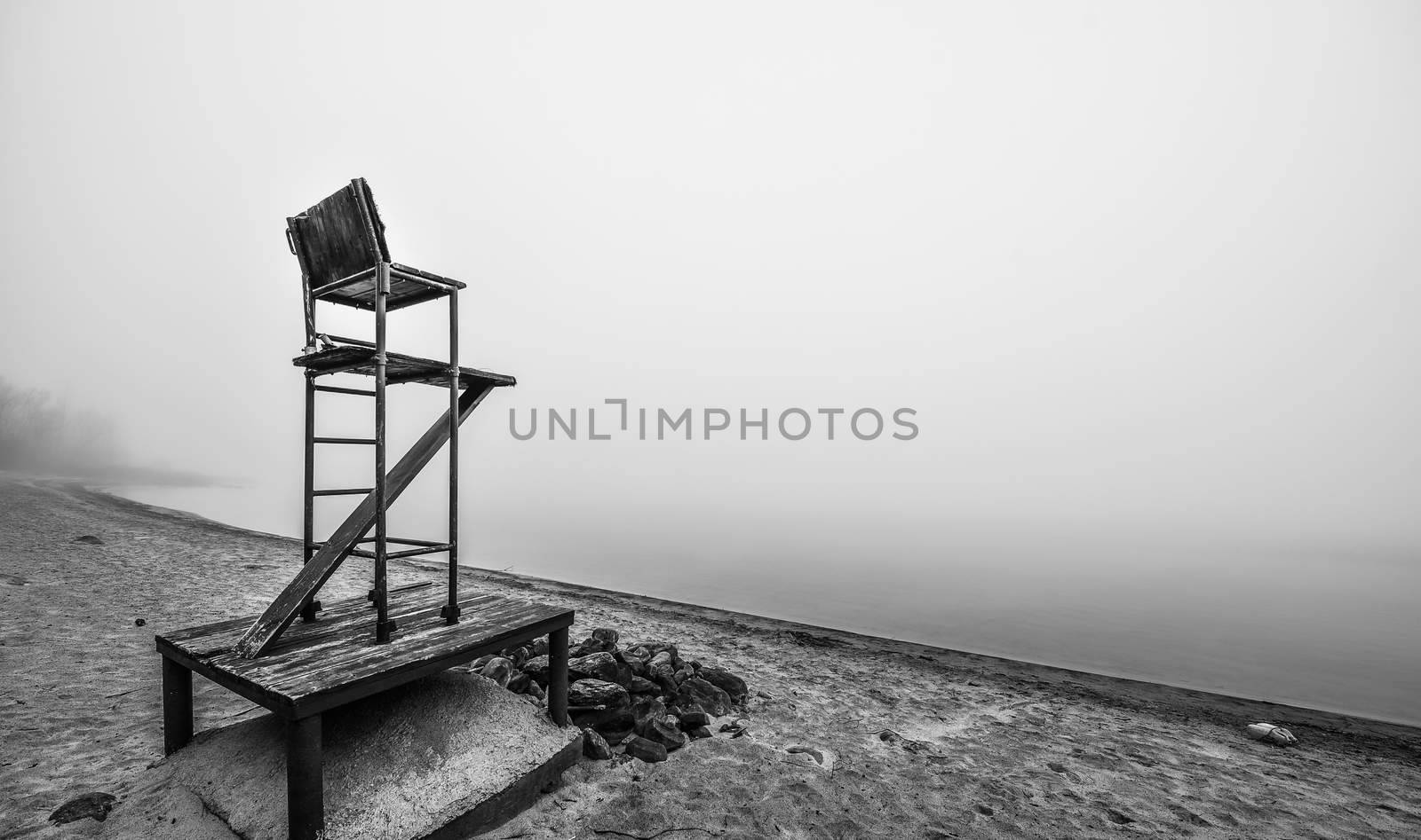 Black & white of lonely lifeguard seat stands empty in the fog on a November beach in Ontario Canada.