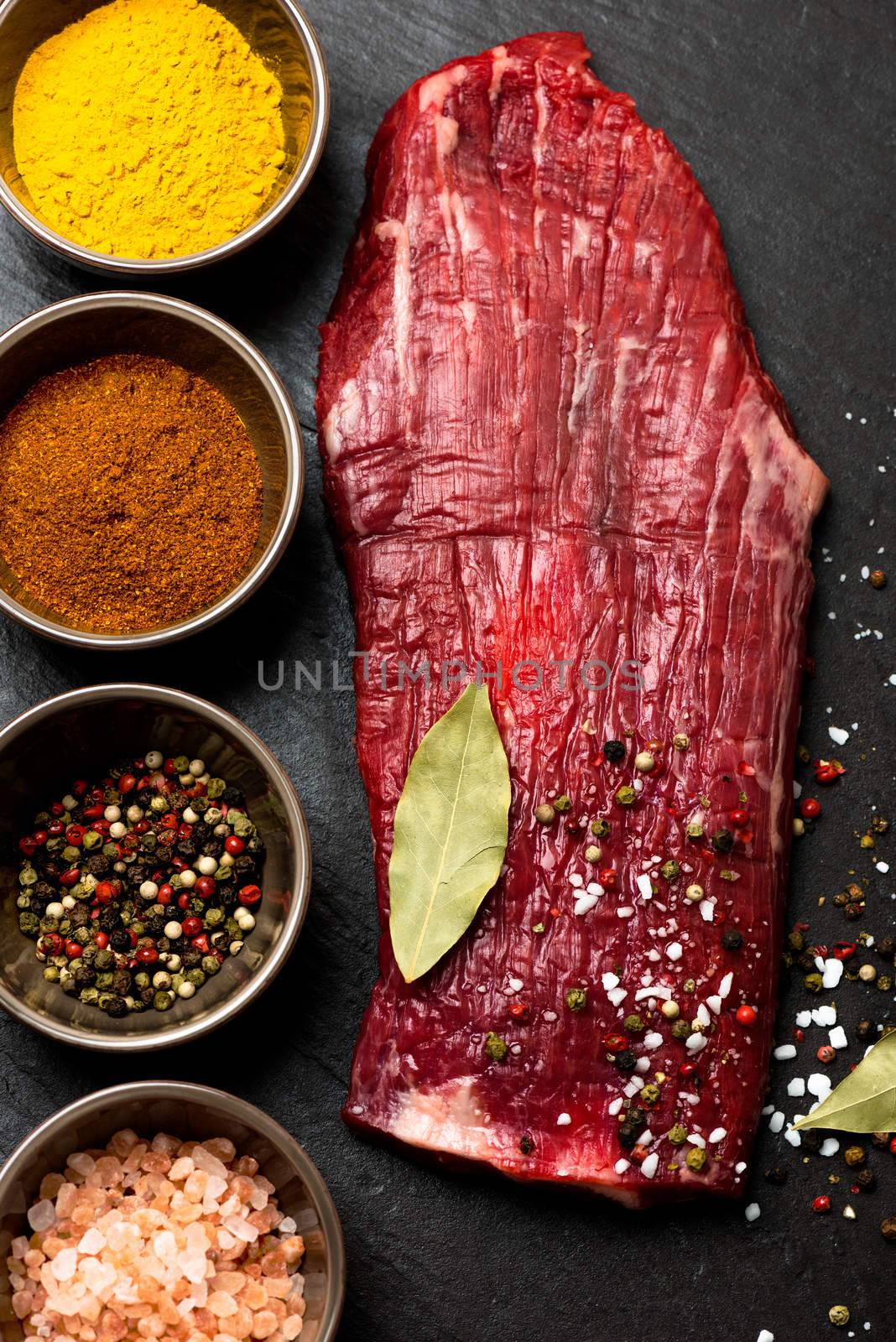 Spices in bowls and raw flank steak on stone background