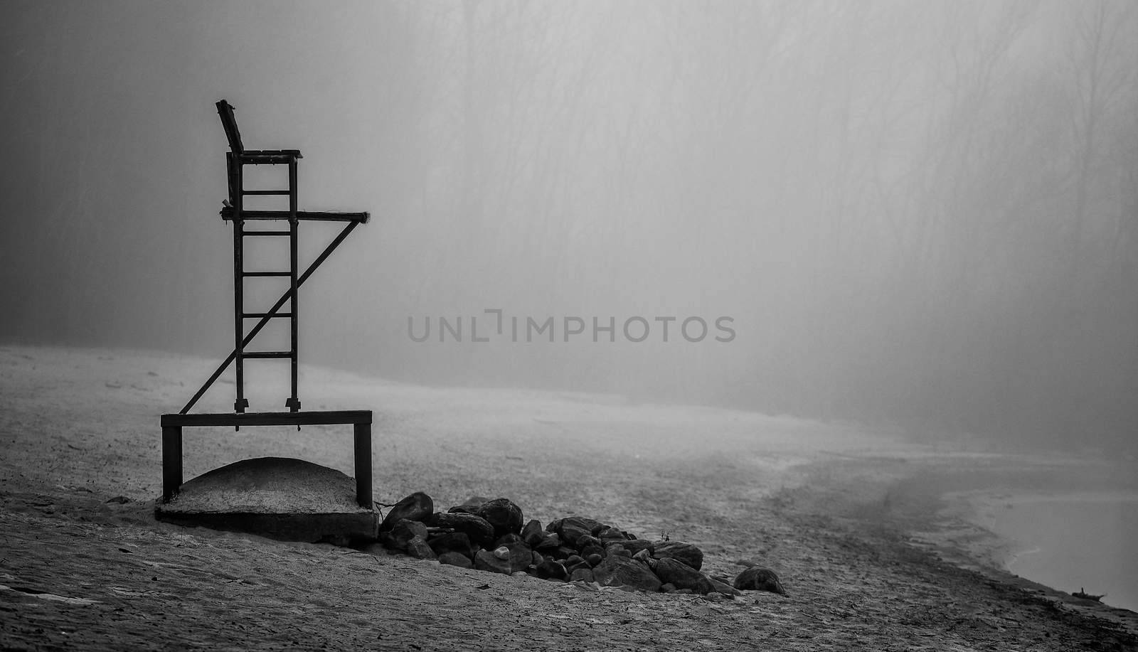 Black & white of lonely lifeguard seat stands empty in the fog on a November beach in Ontario Canada.