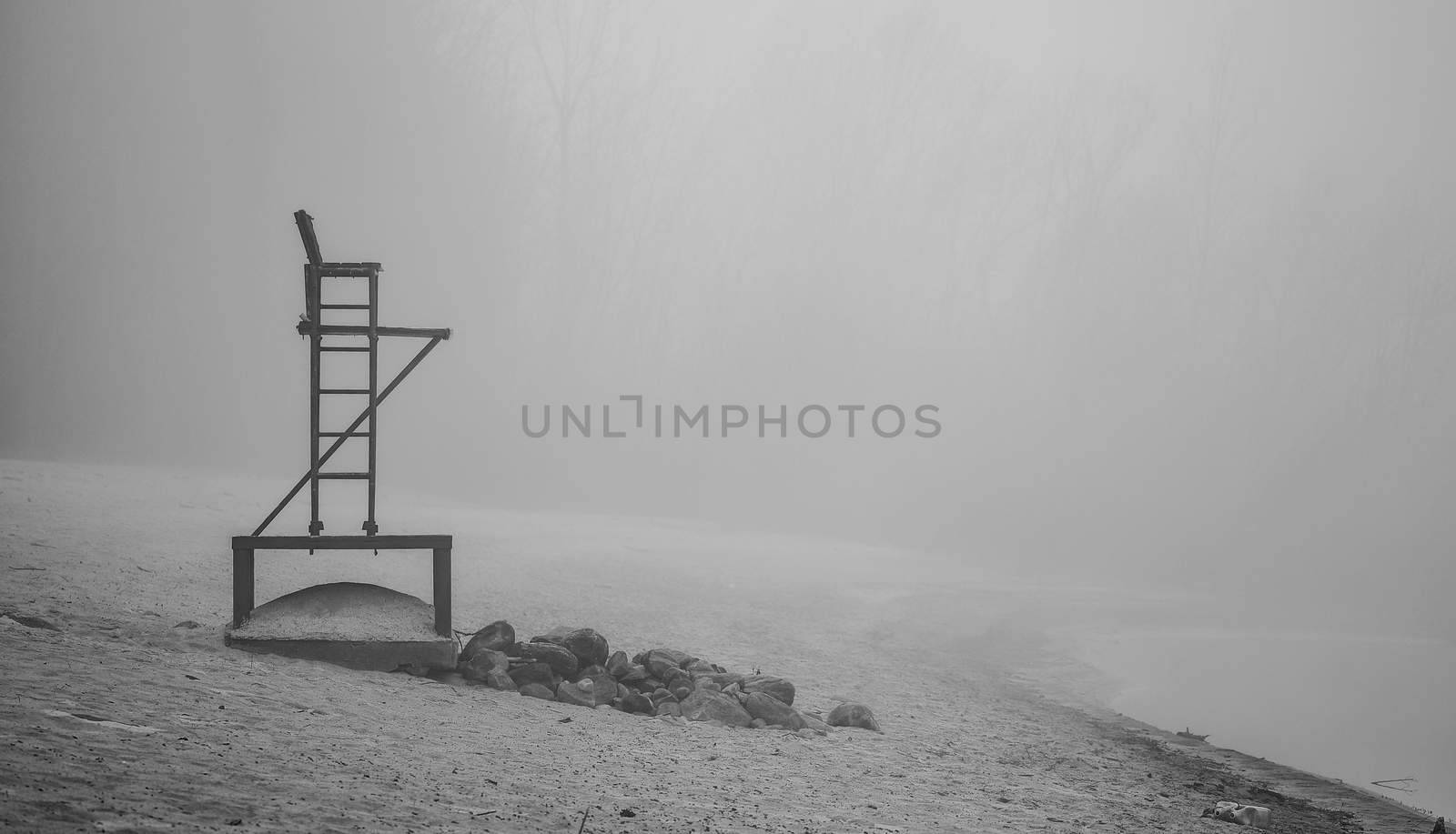 Black & white of lonely lifeguard seat stands empty in the fog on a November beach in Ontario Canada.