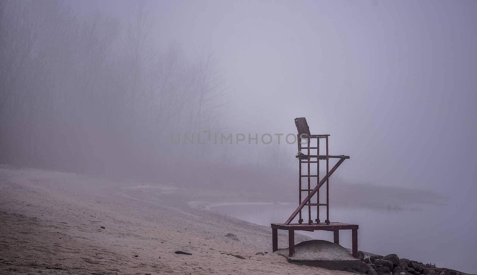 A lonely lifeguard seat stands empty in the fog on a November beach in Ontario Canada.