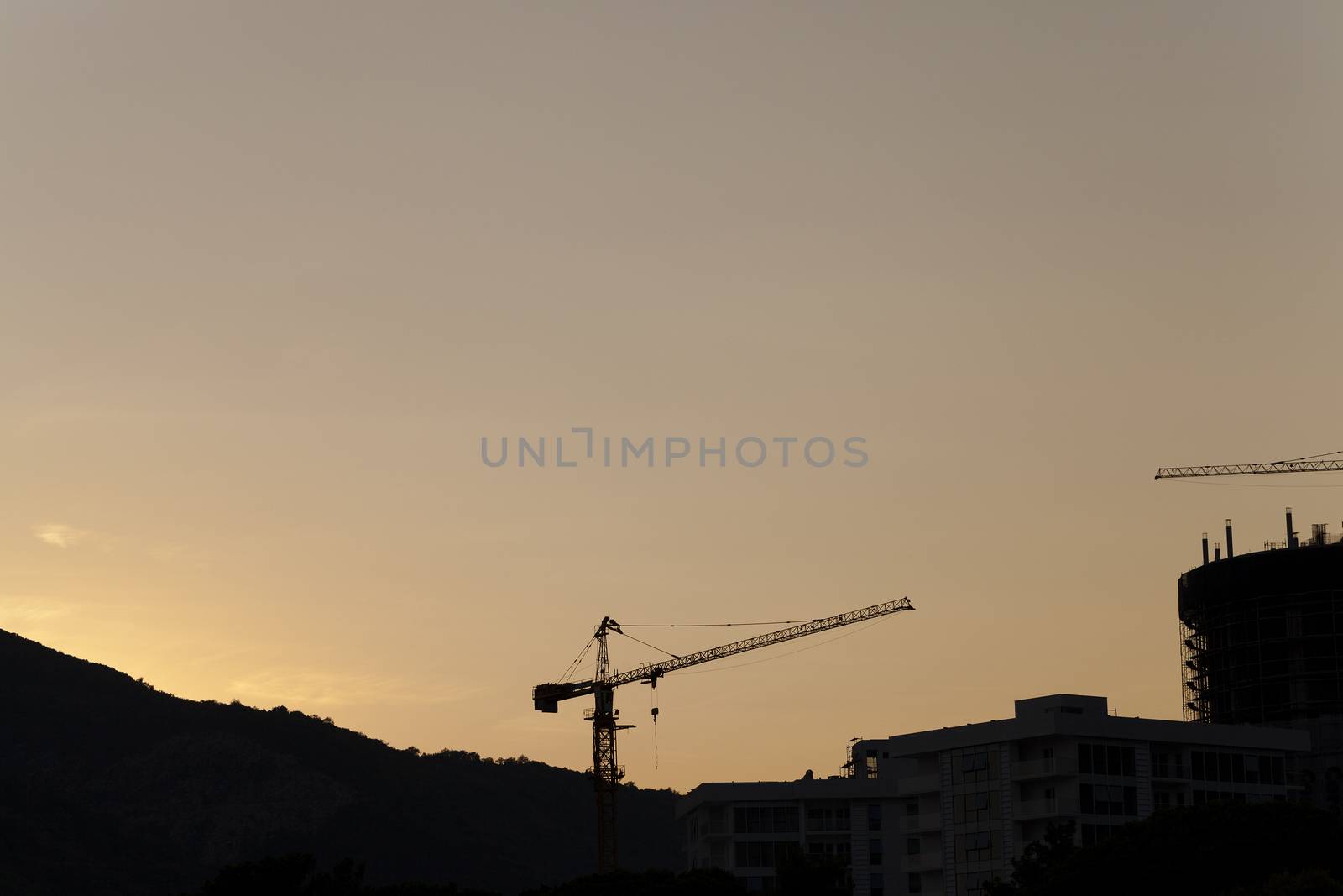  the photograph shows two construction cranes in housing starts. Sunset. In the background mountains.