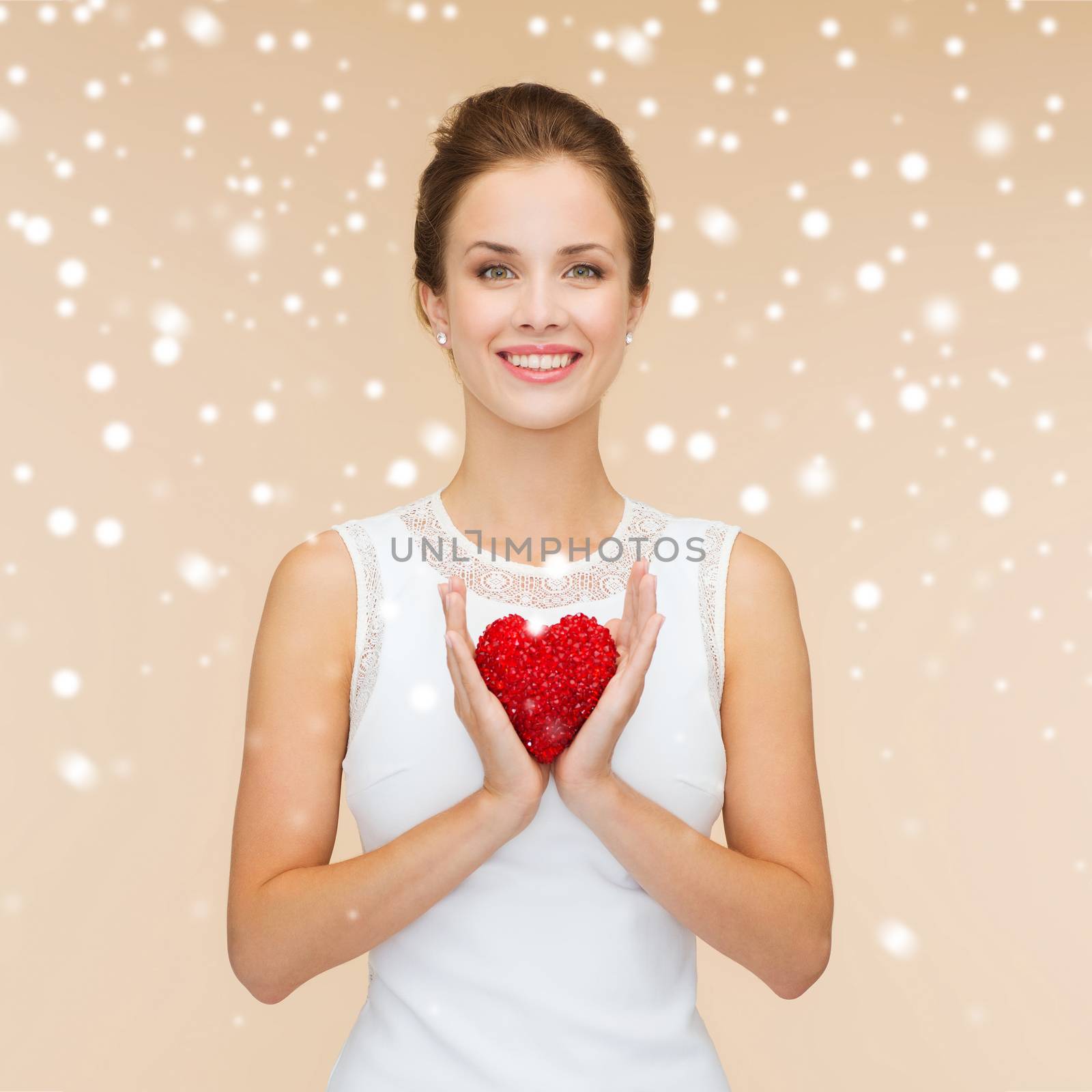 happiness, health, charity and love concept - smiling woman in white dress with red heart over beige background over beige background and snow